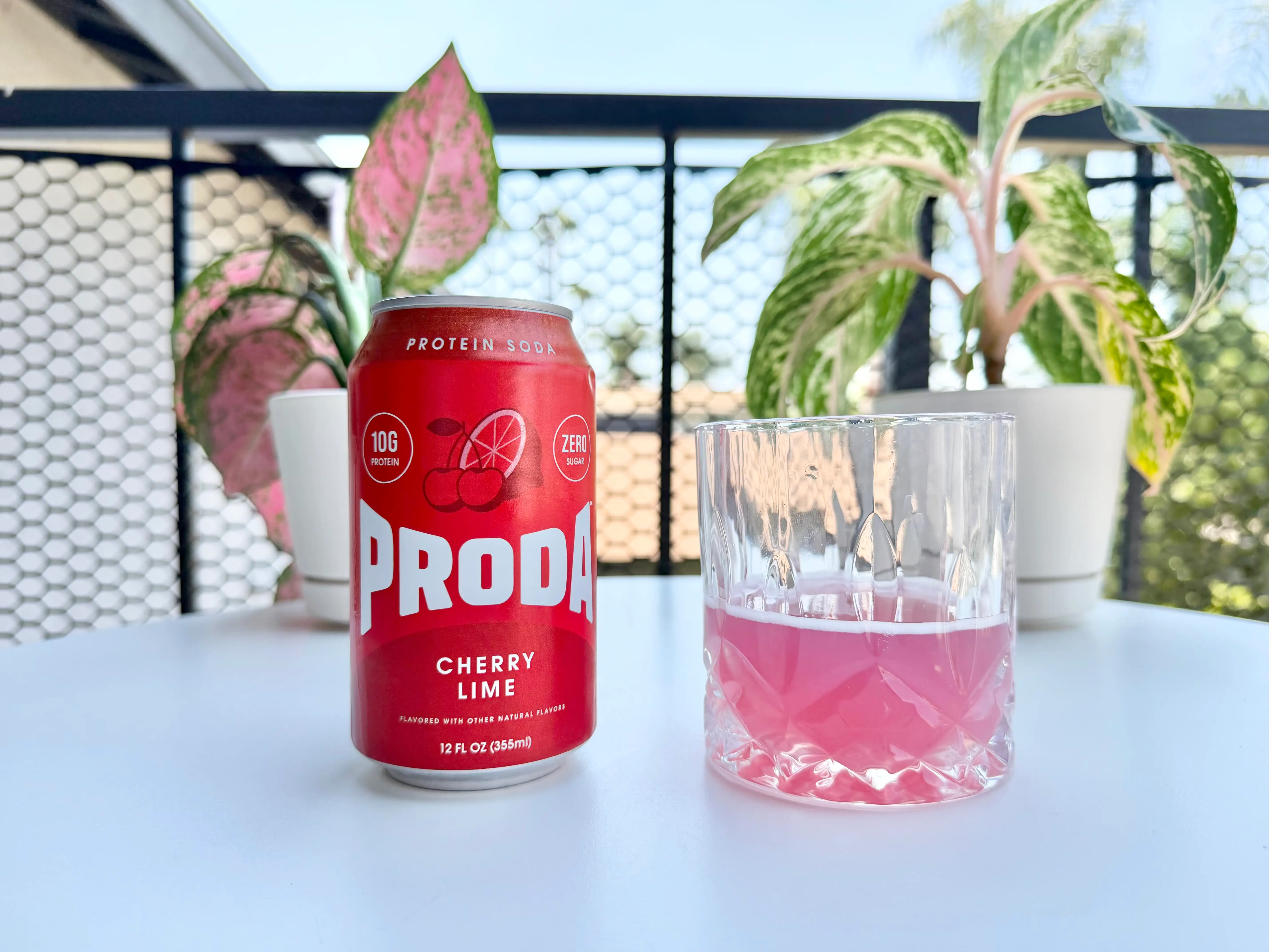 Can of Proda cherry protein soda next to glass of soda, pink liquid