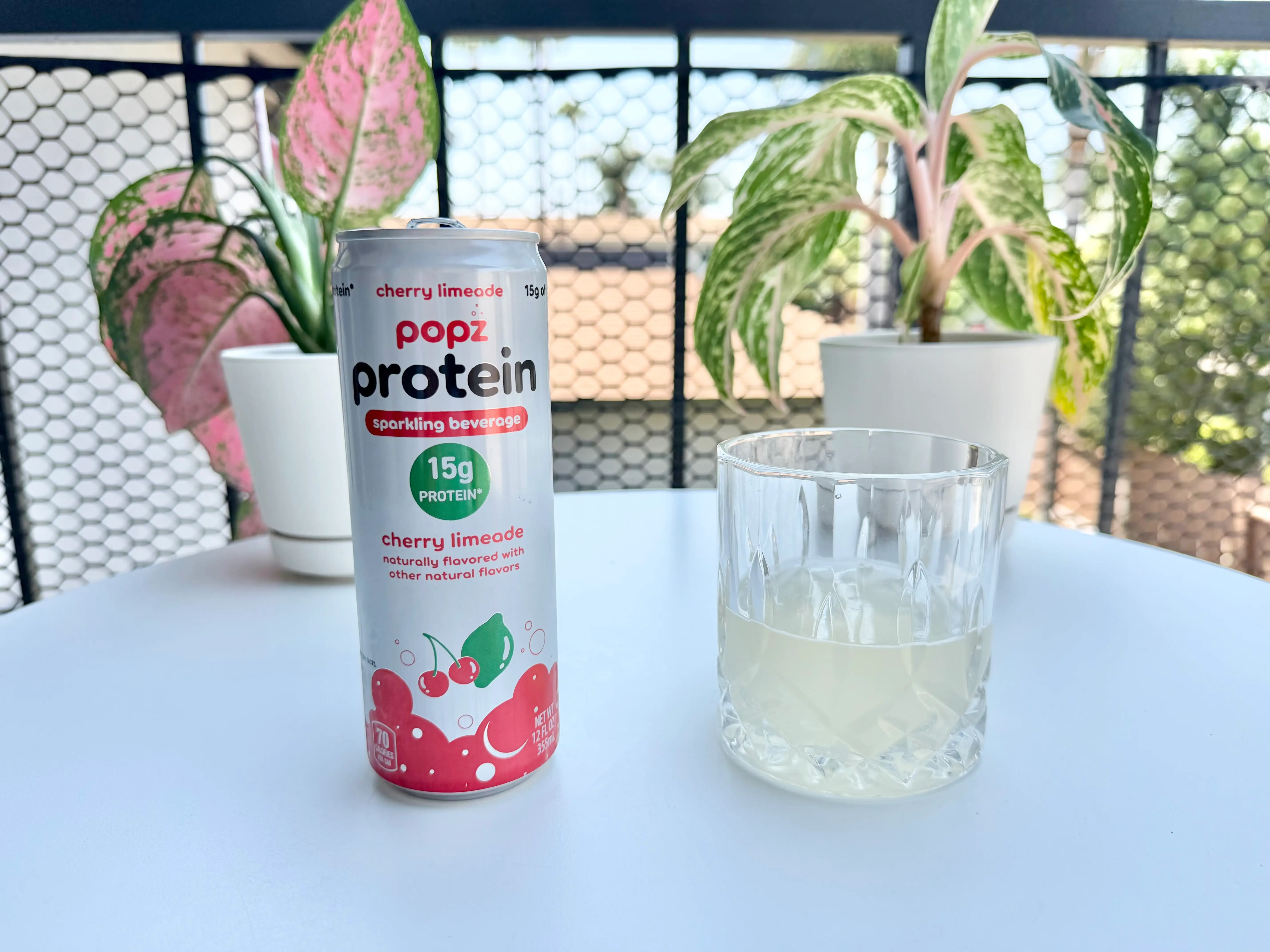 Can of Popz cherry protein soda from Aldi next to glass of soda, beige liquid