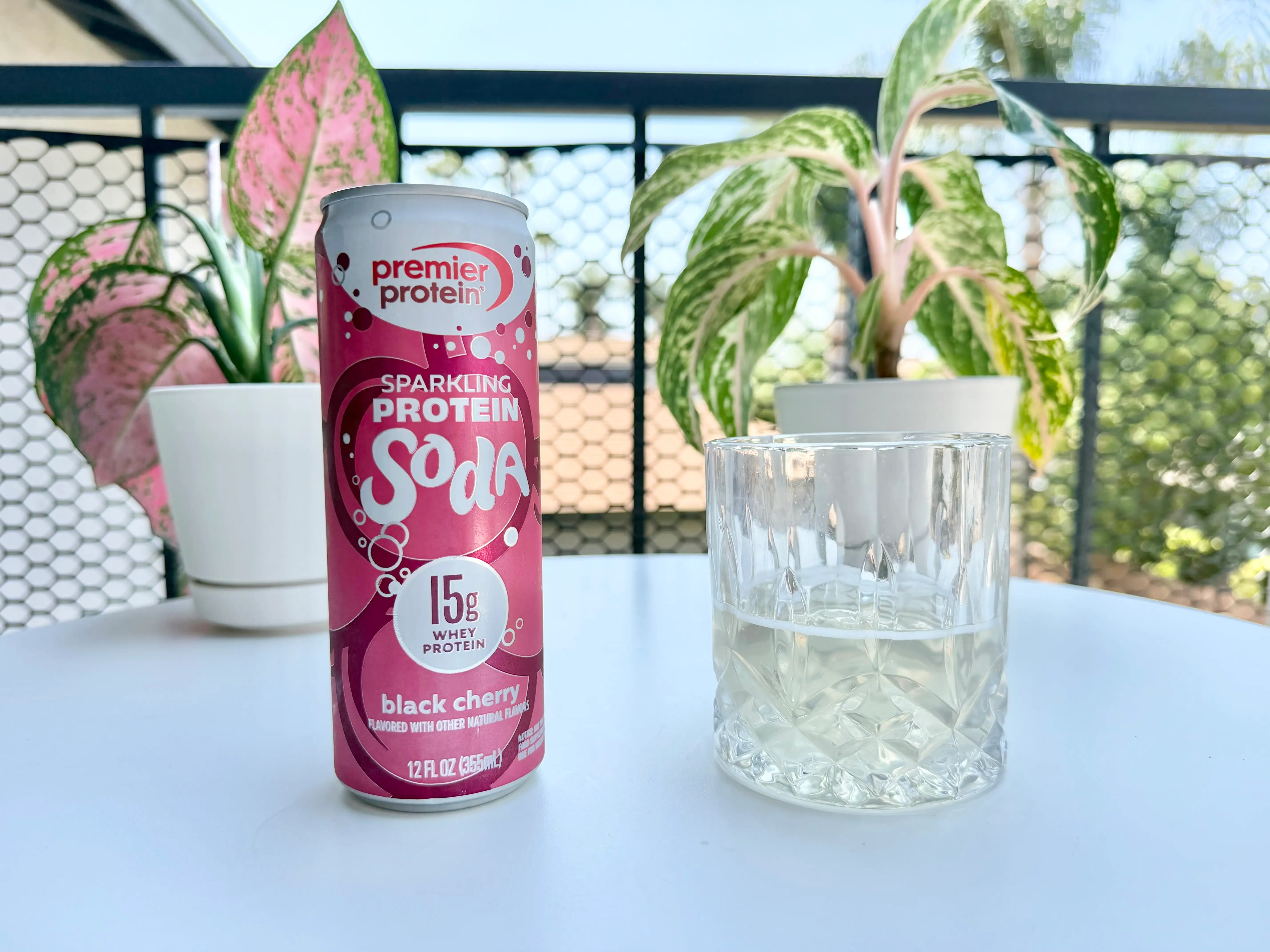 Can of Premier Protein cherry protein soda next to glass of soda, beige liquid