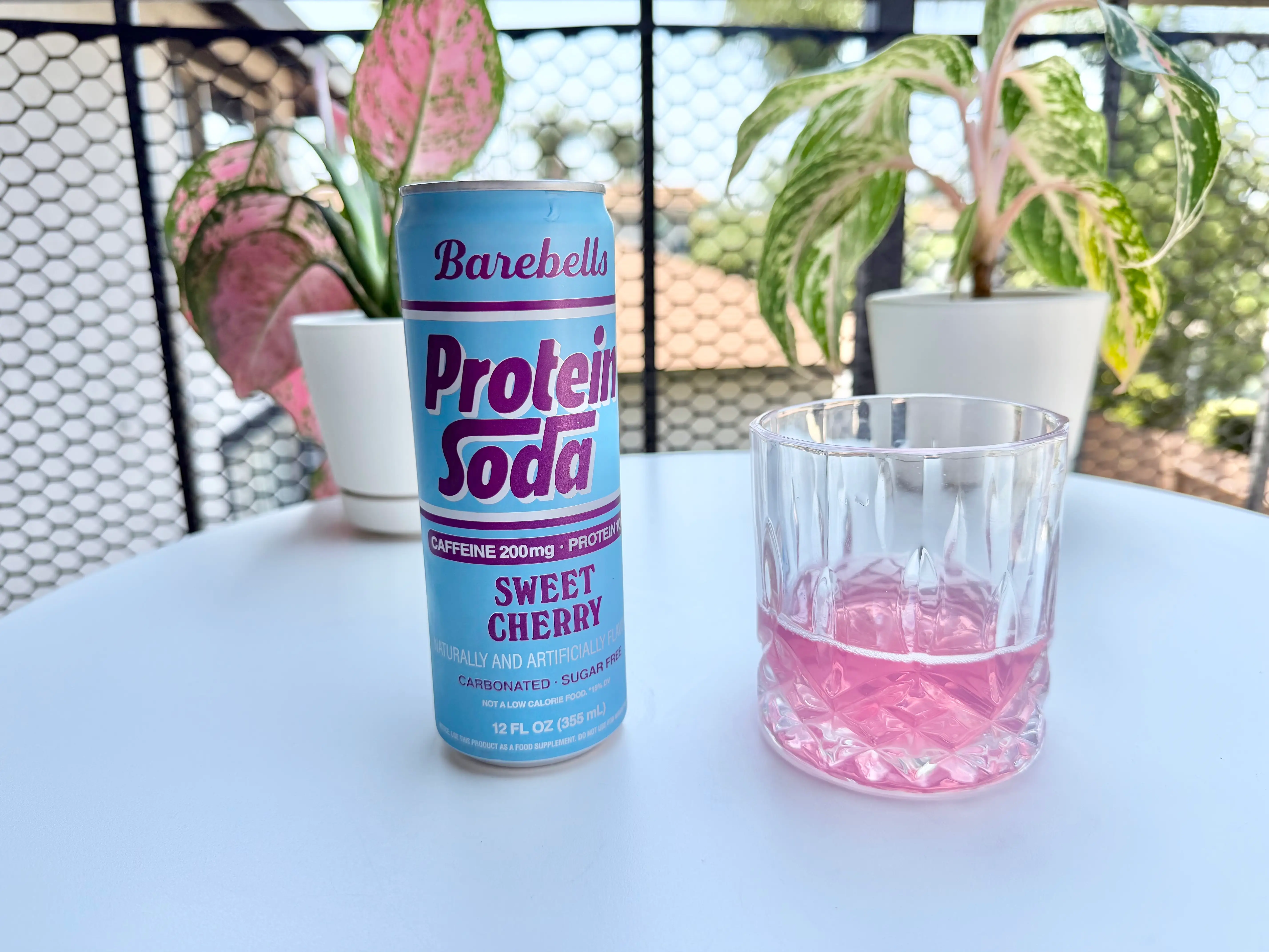 Can of Barebells cherry protein soda next to glass of soda, pink liquid