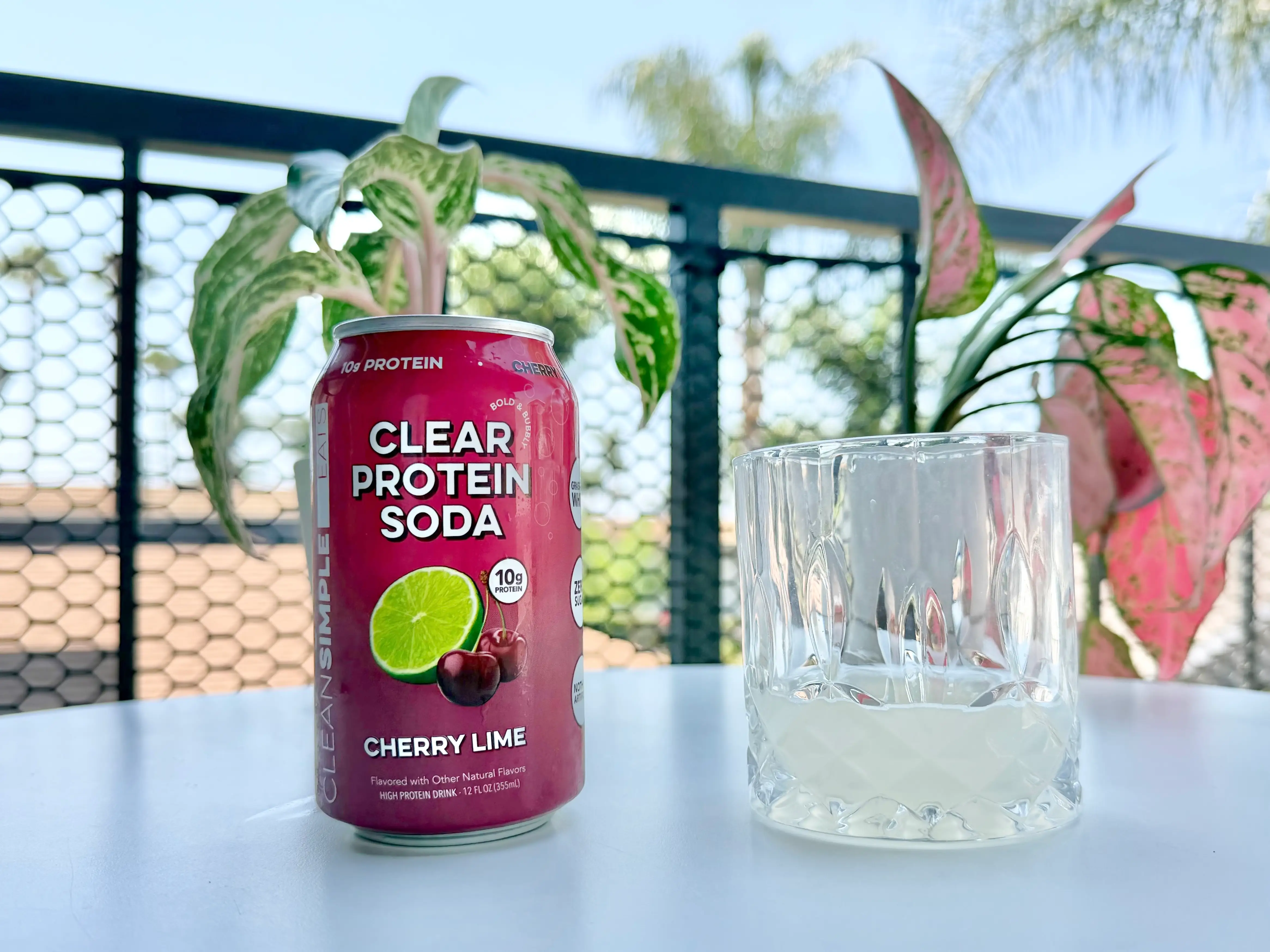 Can of Clean Simple Eats cherry protein soda next to glass of soda, pink liquid