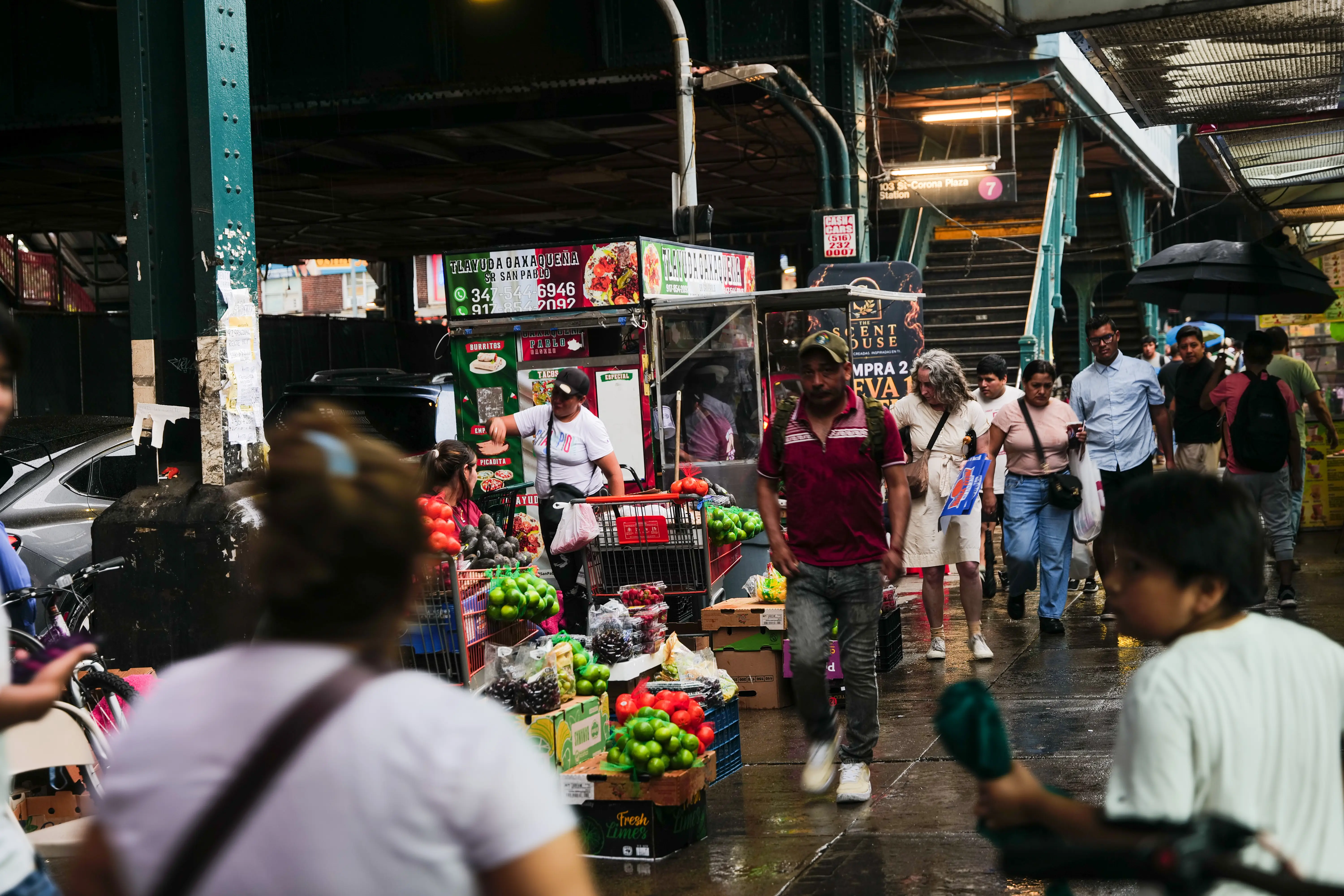 People walk on a busy sidewalk under a bridge in New York.