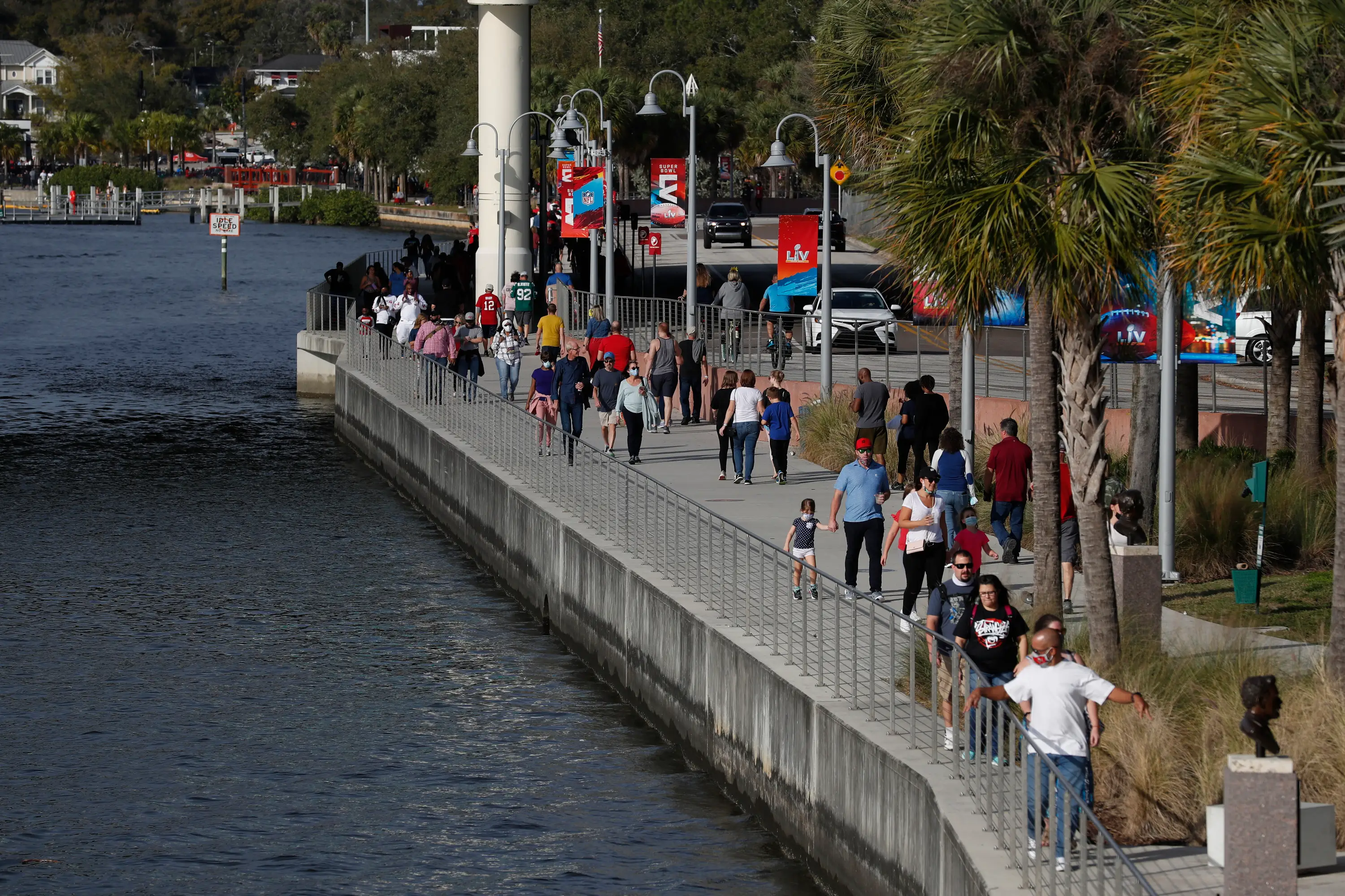 Pedestrians walk along a sidewalk next to water.