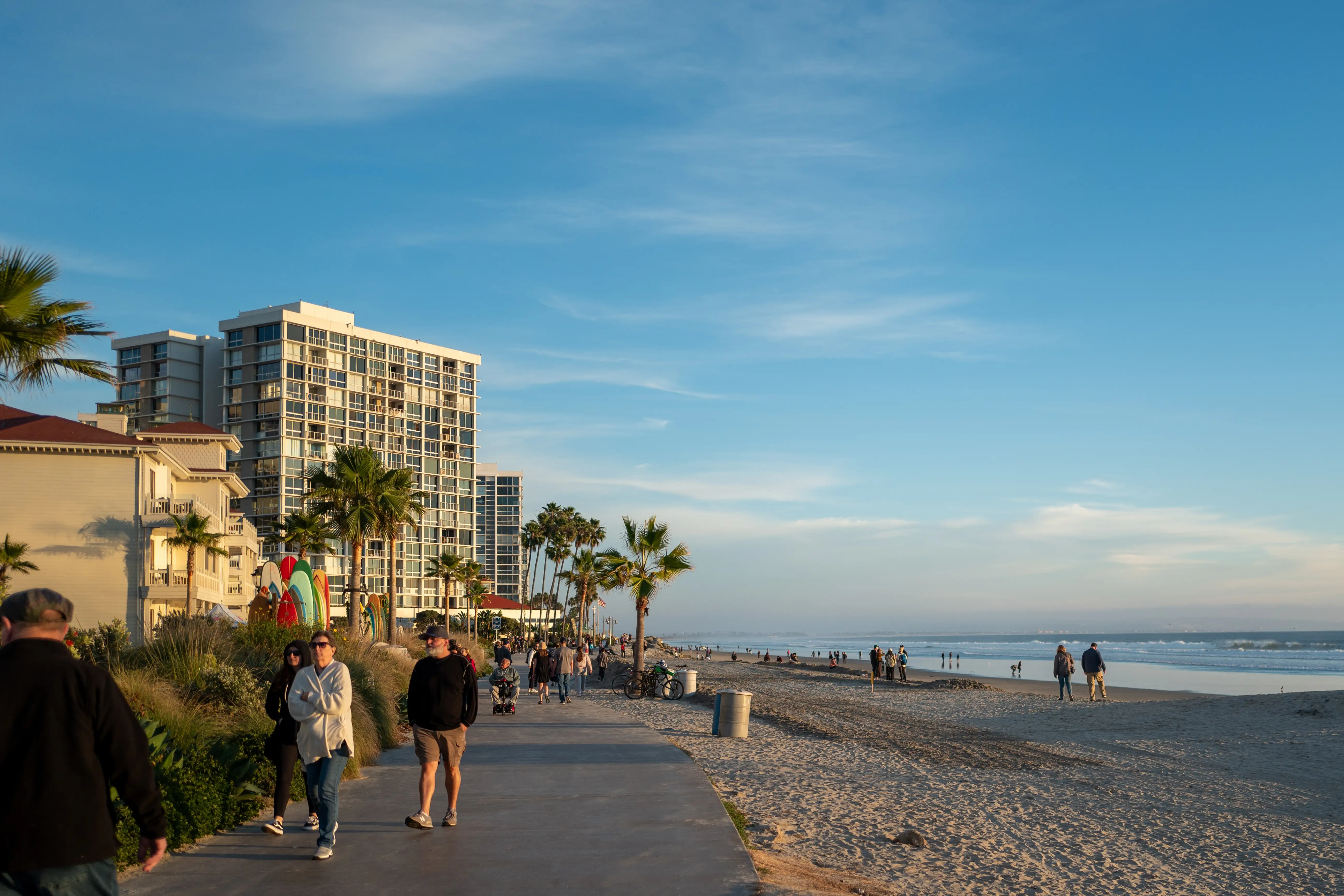Pedestrians walk along a path next to a sunny beach.