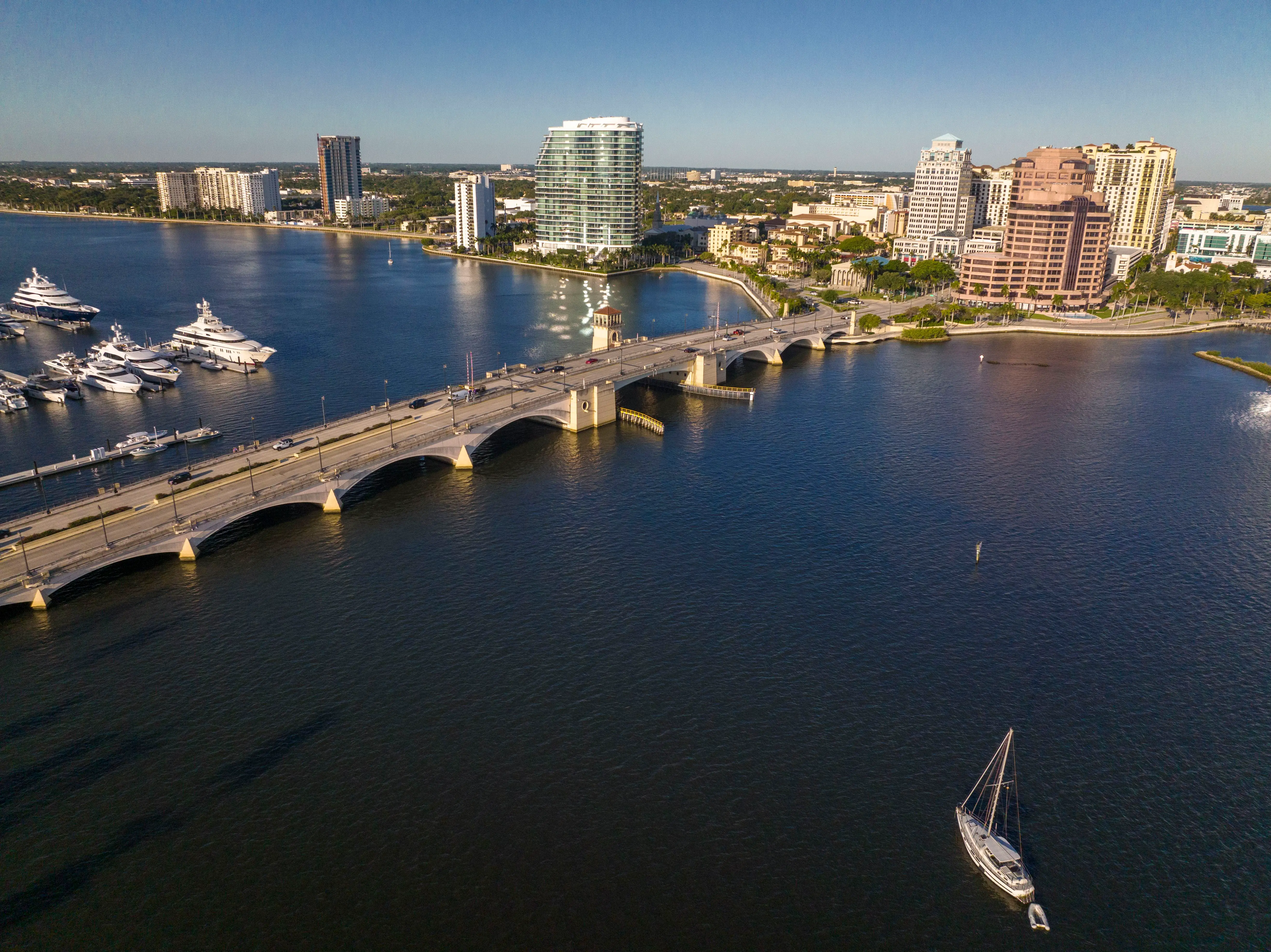 A sailboat approaches a drawbridge and nearby downtown area.