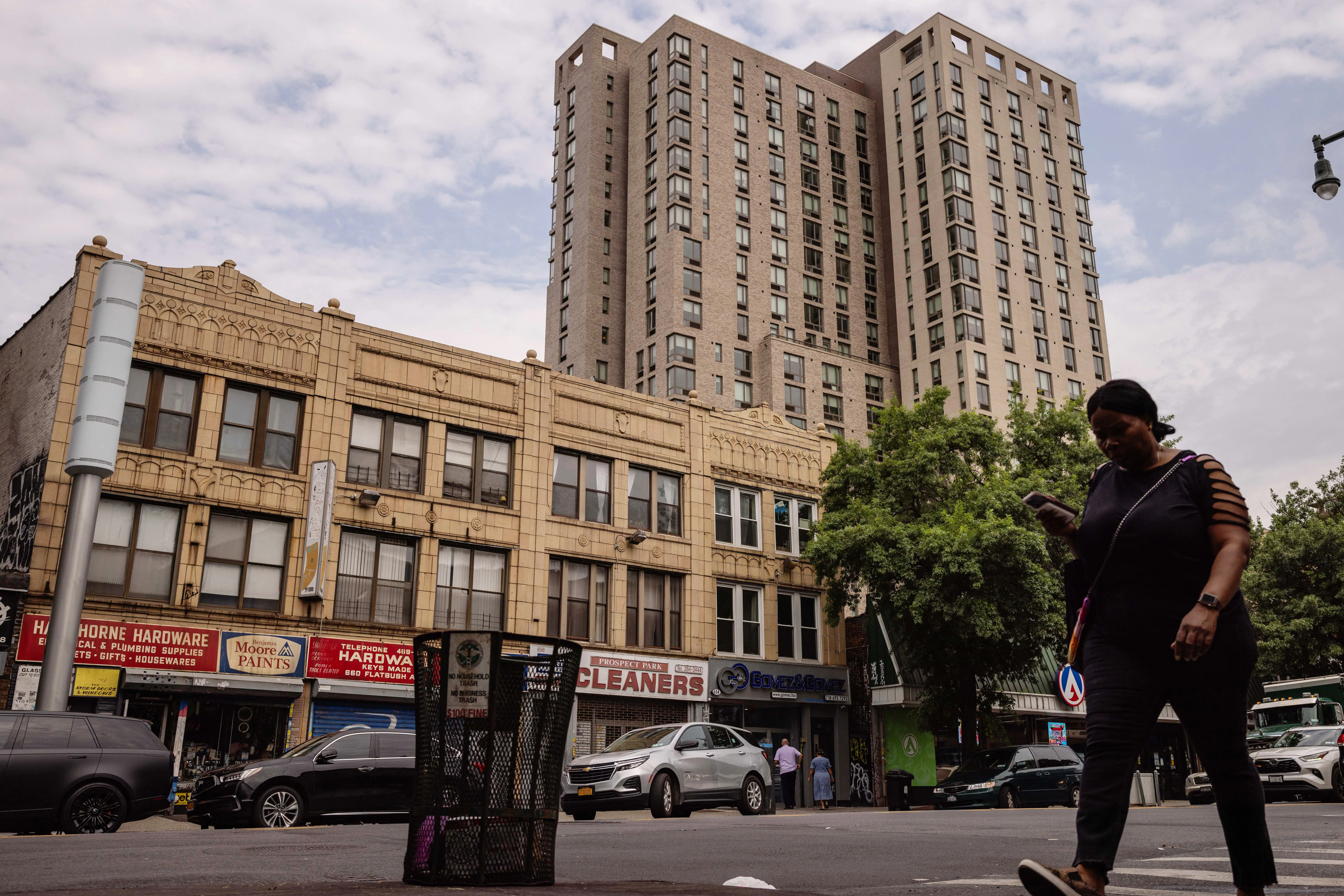 A woman walks on a sidewalk with two brick buildings in the background.