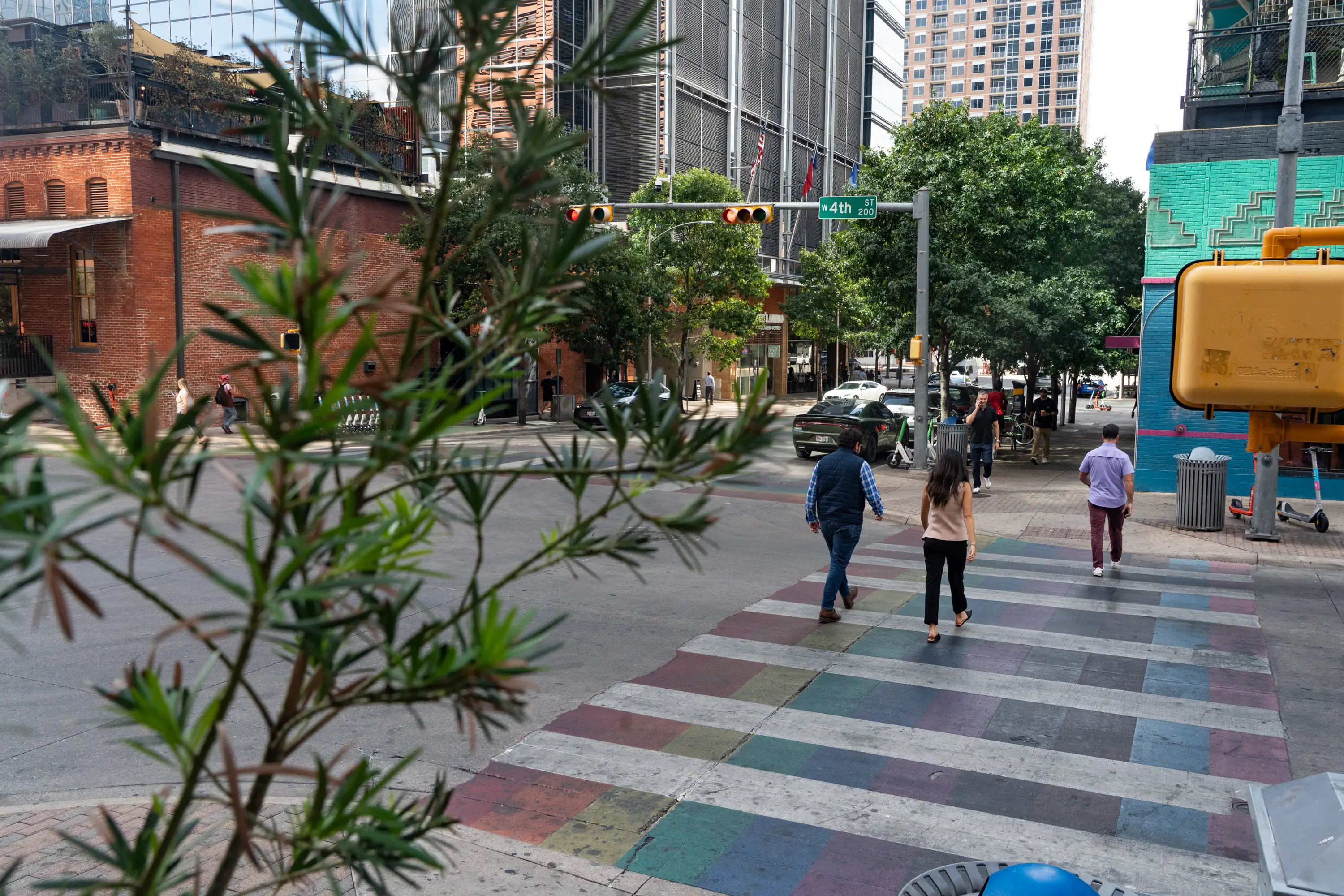 People walk over a rainbow crosswalk in the downtown area of a city.