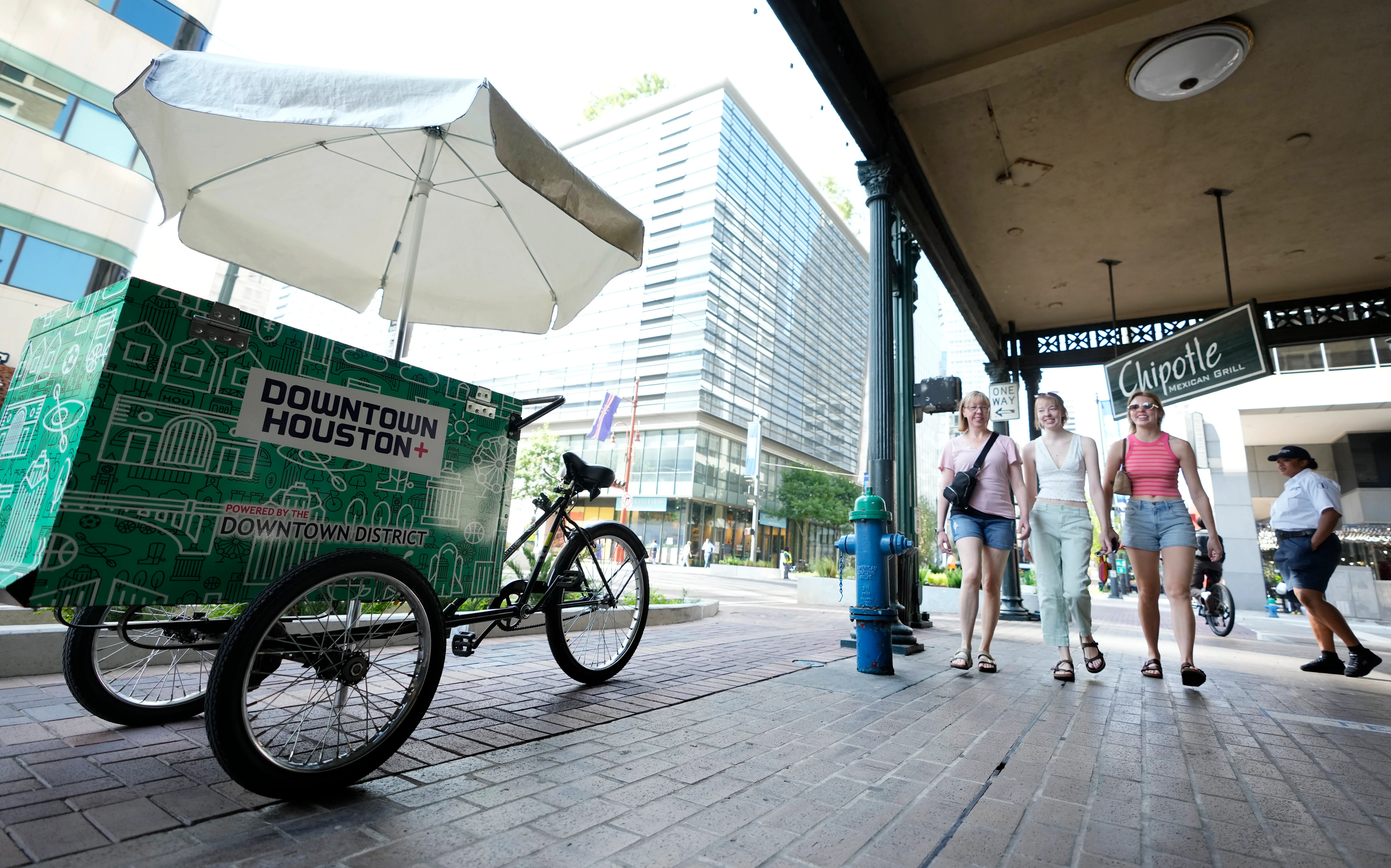 People walk on a sidewalk next to a vendor cart that says 
