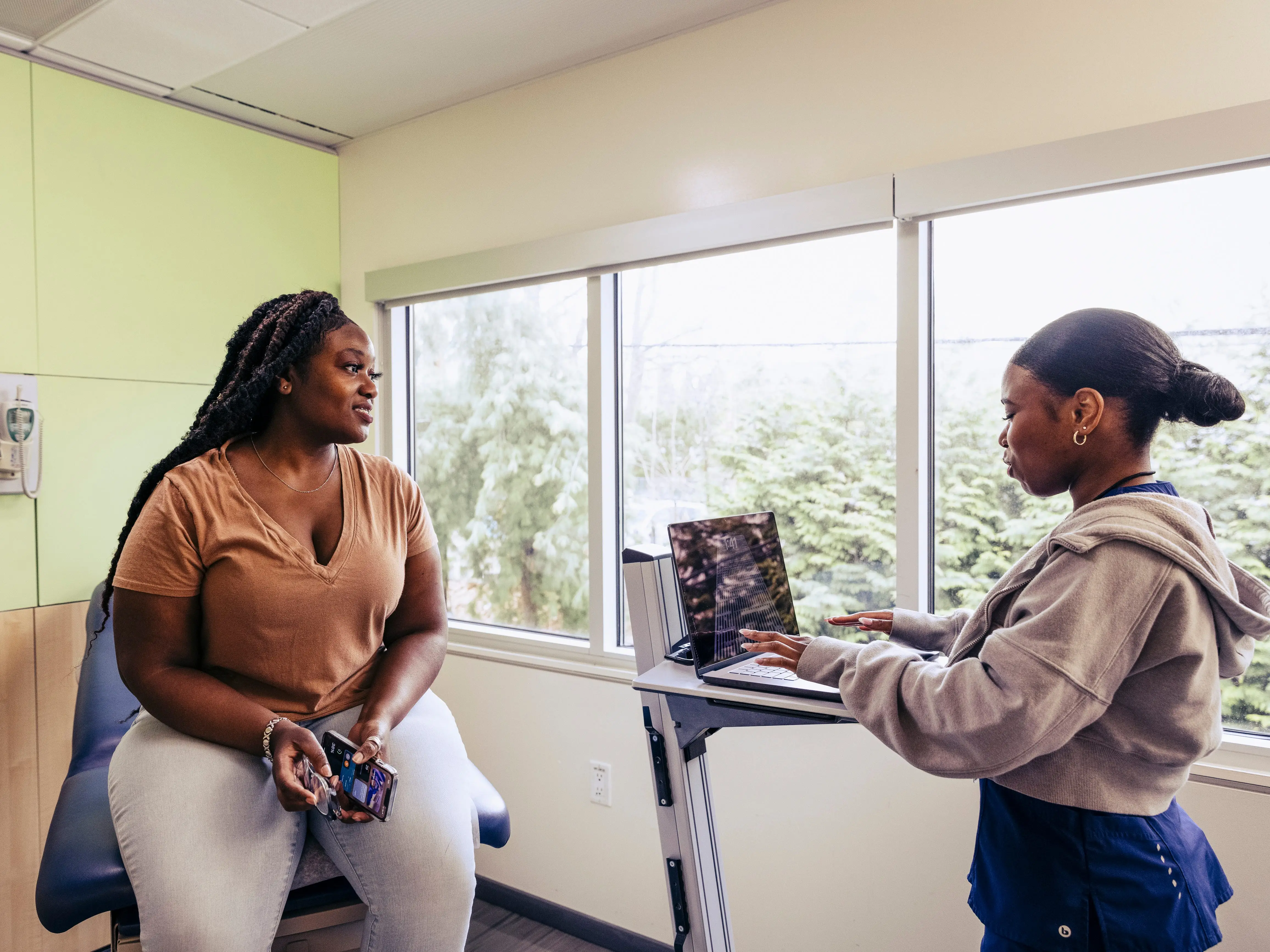 A healthcare worker is using a laptop while a patient looks at her