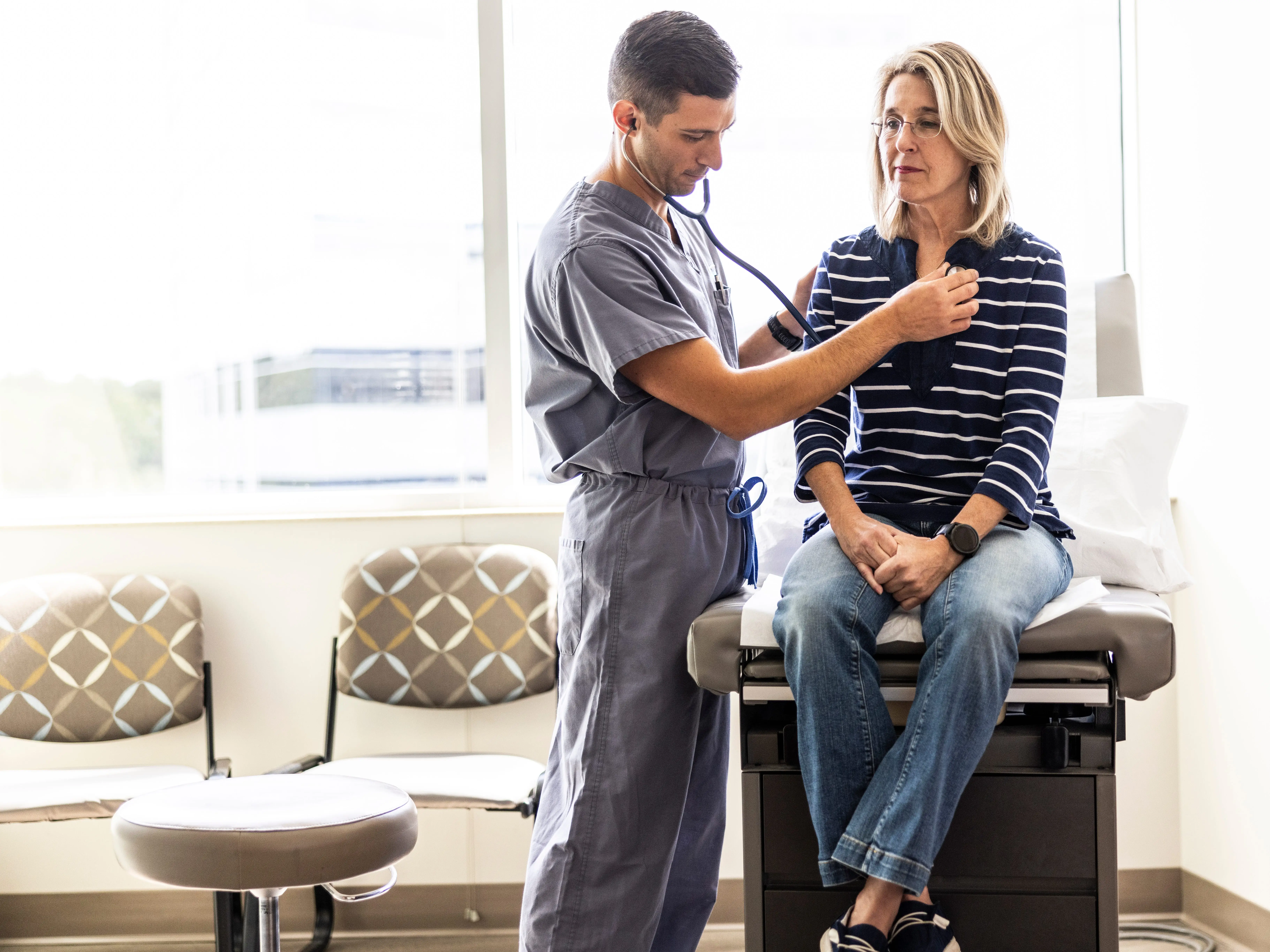 A healthcare worker in scrubs uses a stethoscope on a seated person
