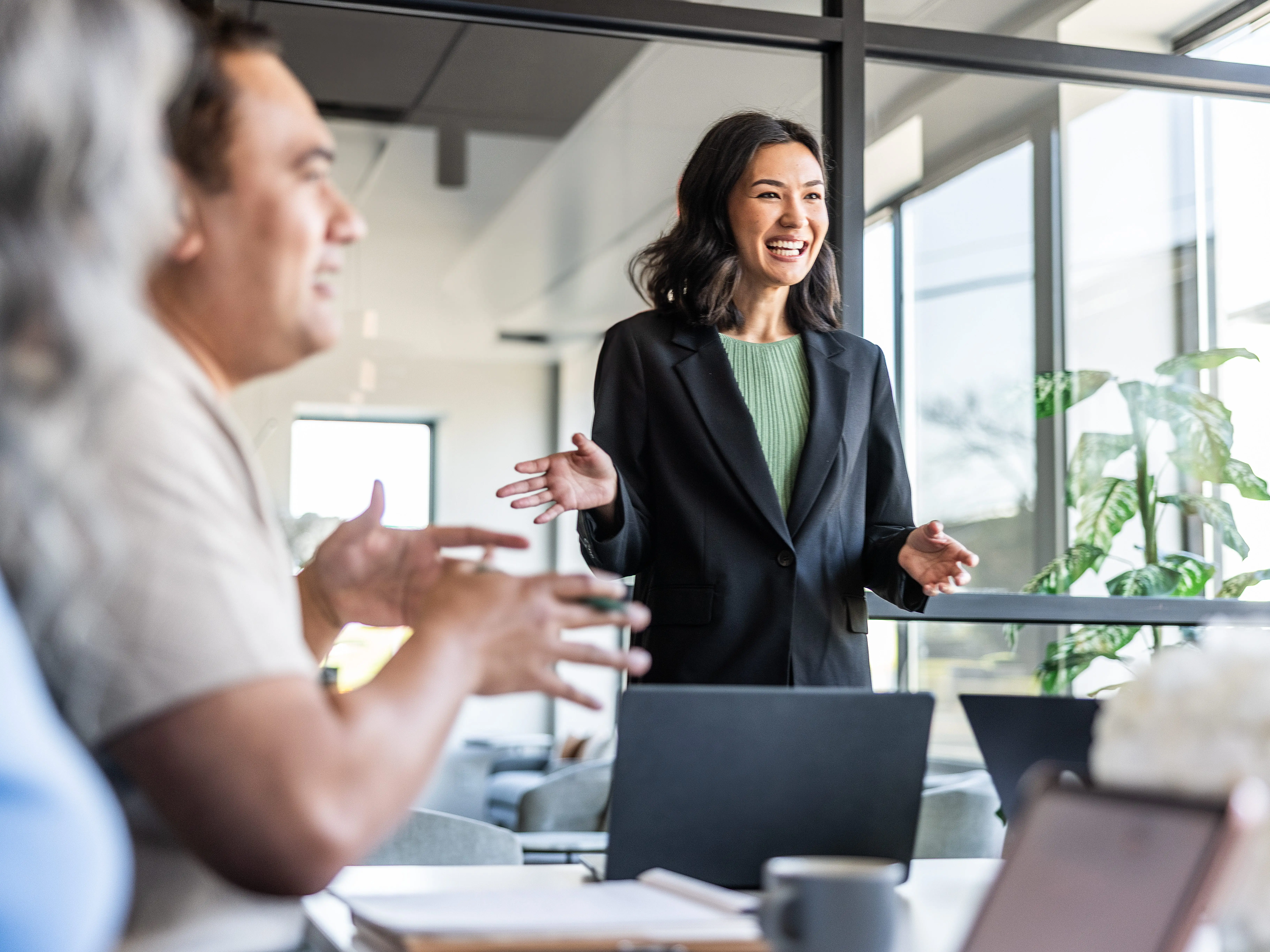 A smiling presenter in a blazer speaks to colleagues in an office meeting