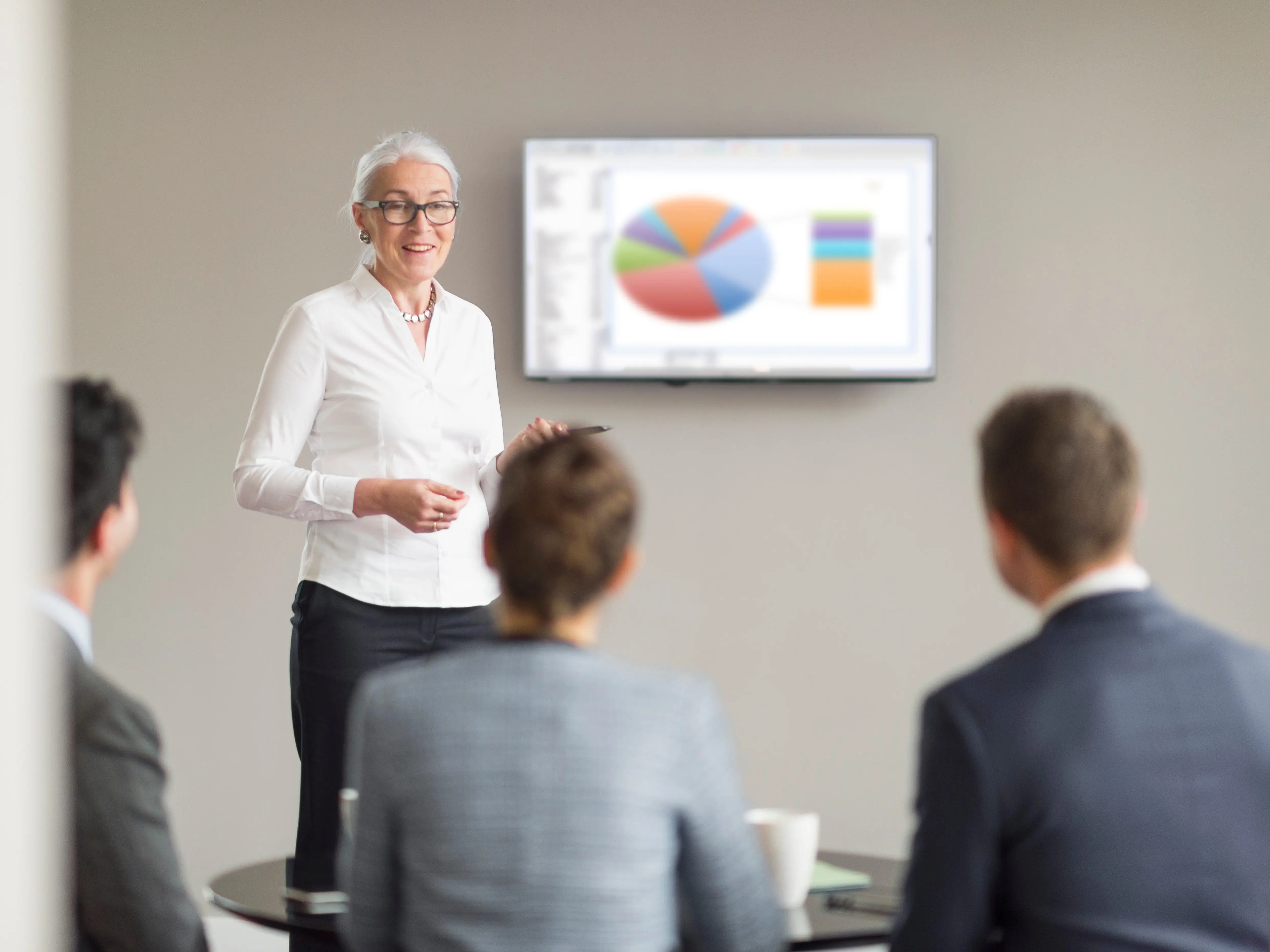 A person presenting to people who are seated, with a chart displayed on a screen behind them