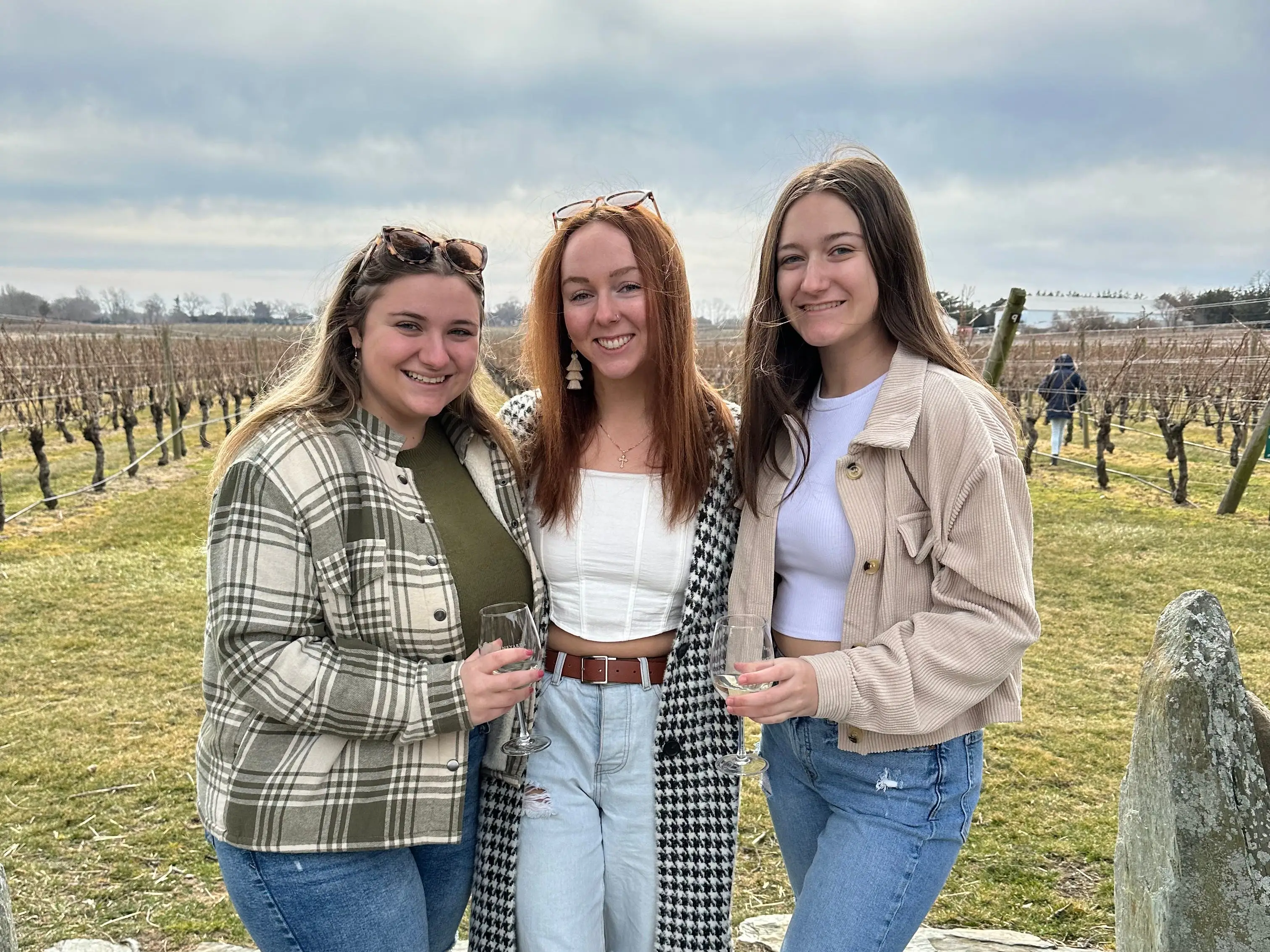 The writer and two friends wearing jackets and holding glasses of wine at a vineyard.