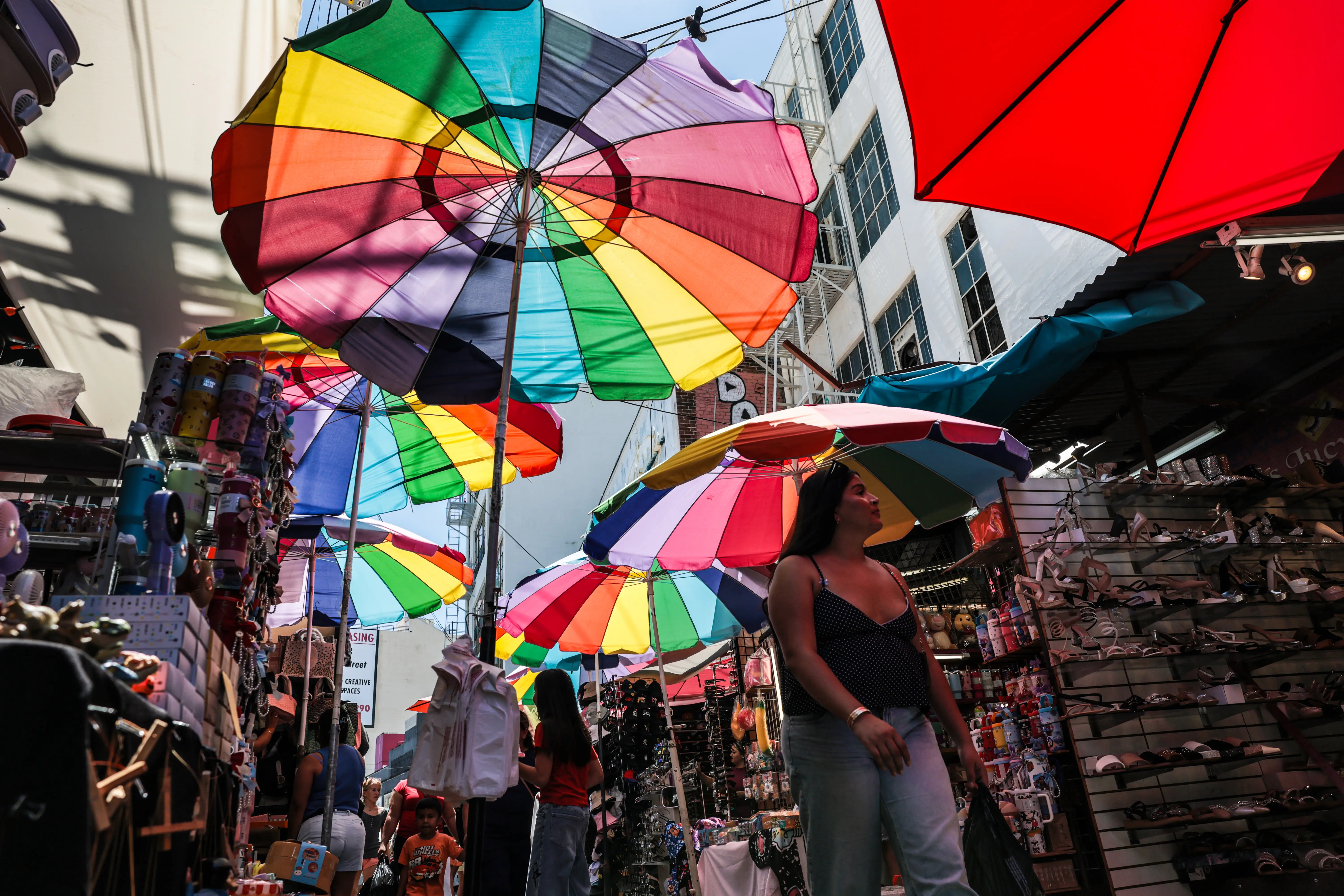 A woman walks through a shopping center with rainbow umbrellas hanging from above.
