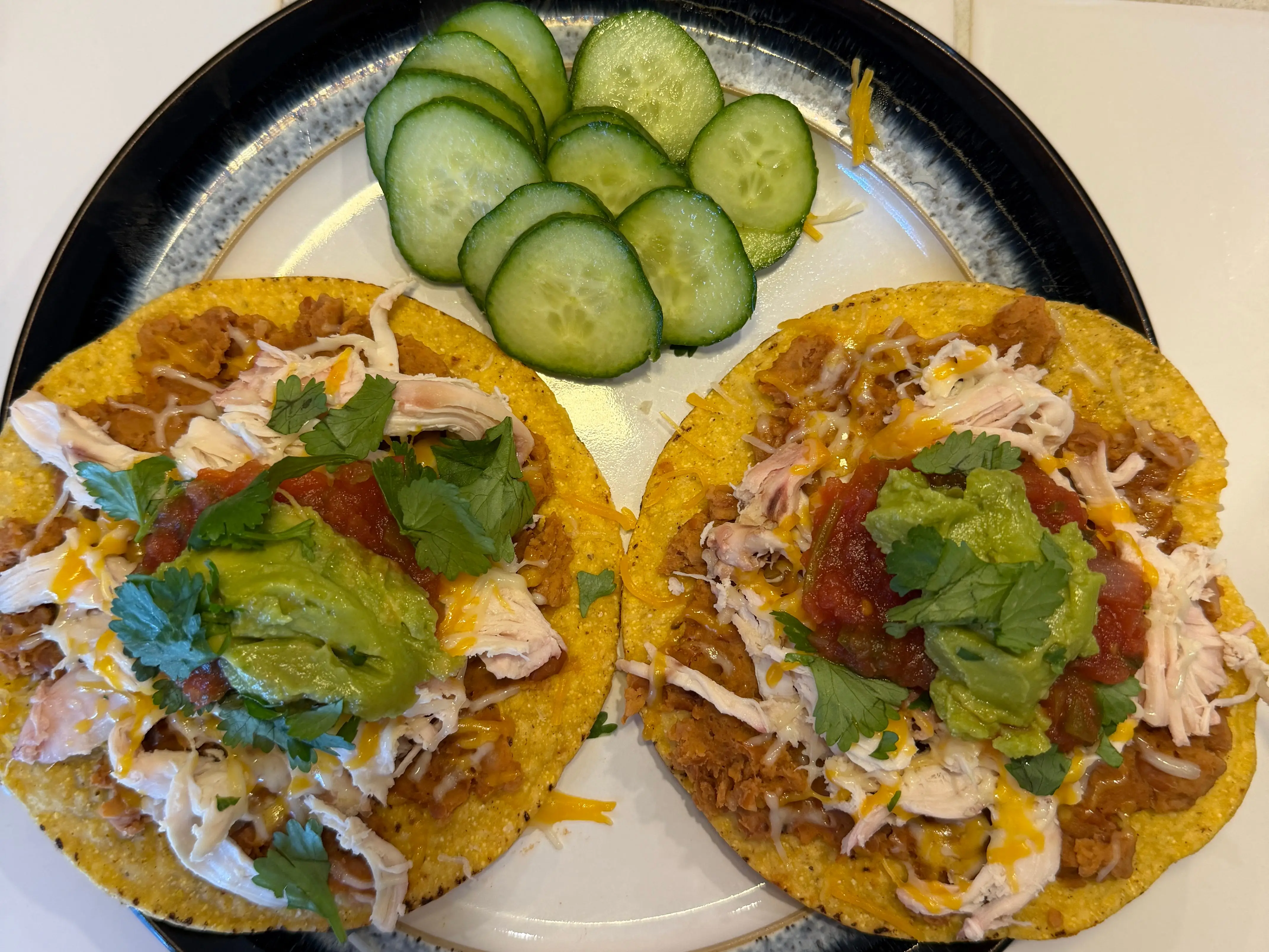 Open-face chicken tostados topped with herbs, next to slcied cucumb