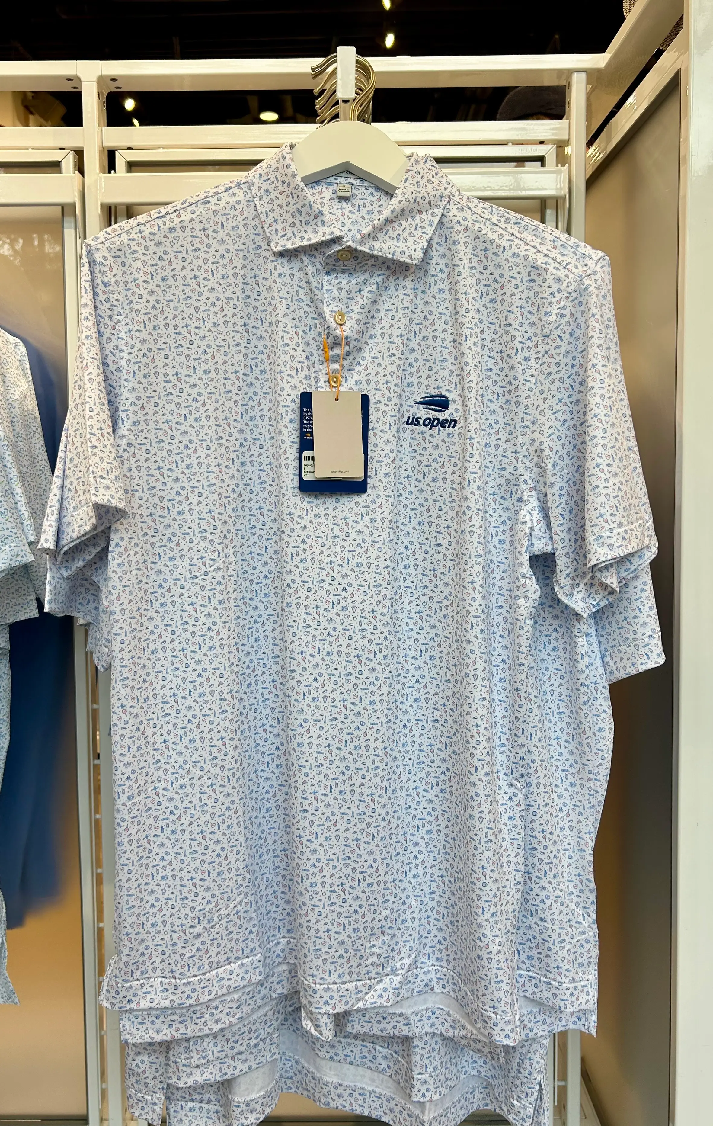 White patterned US Open Peter Millar polo shirt hangs on a retail rack with tags attached.