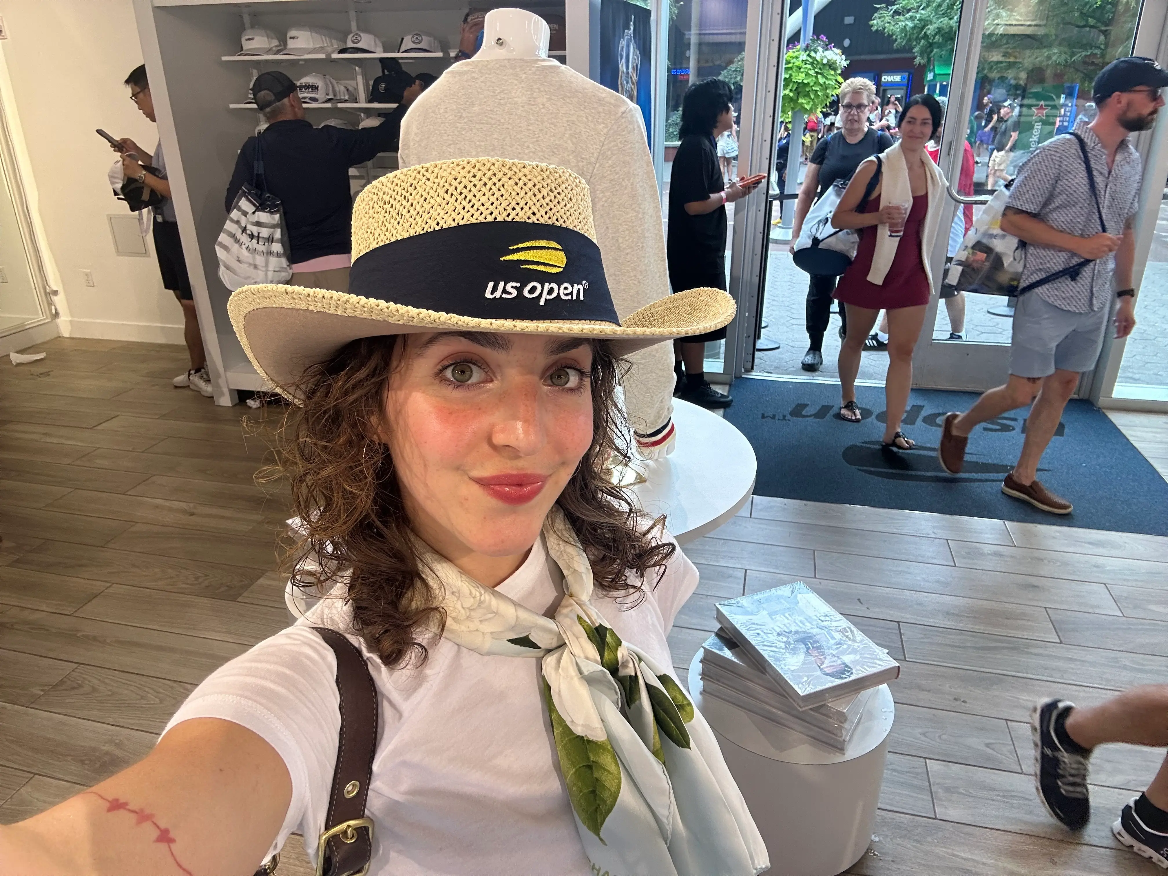 Alice Tecotzky takes a selfie in a merchandise shop while wearing a straw hat with a us open® logo.