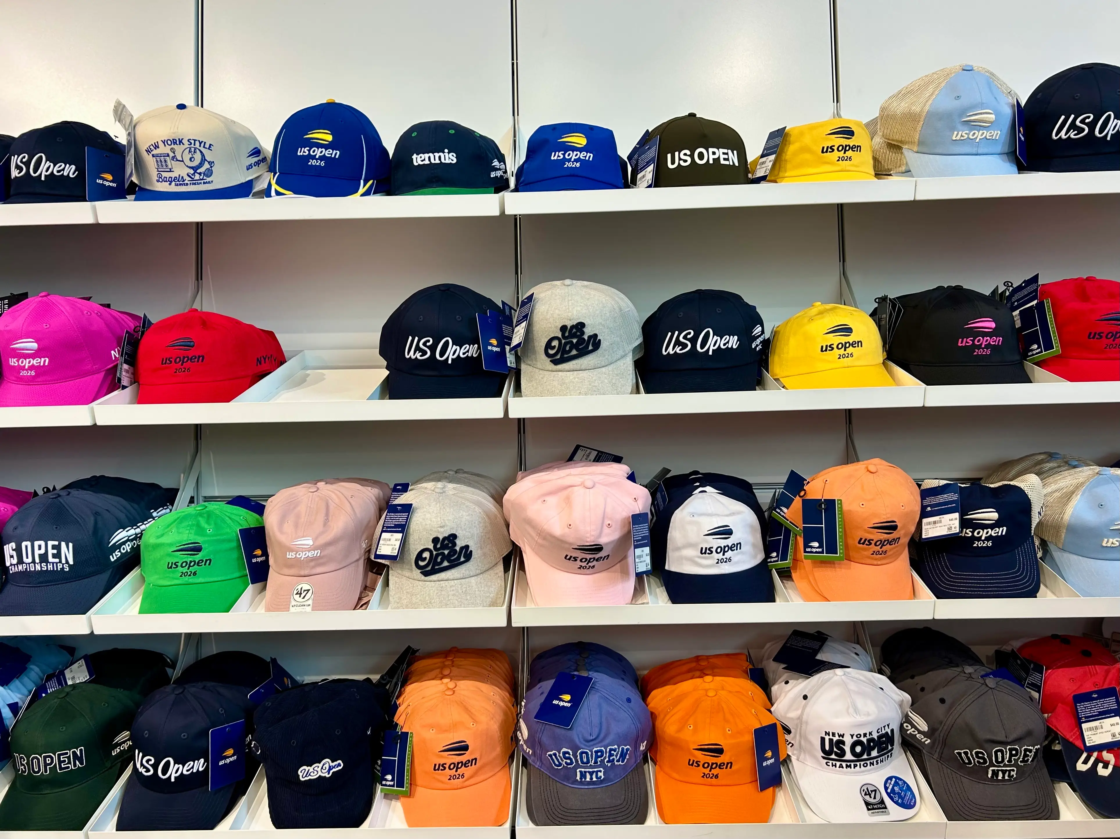 Shelves display colorful US Open tennis caps and tagged merchandise in a retail setting.