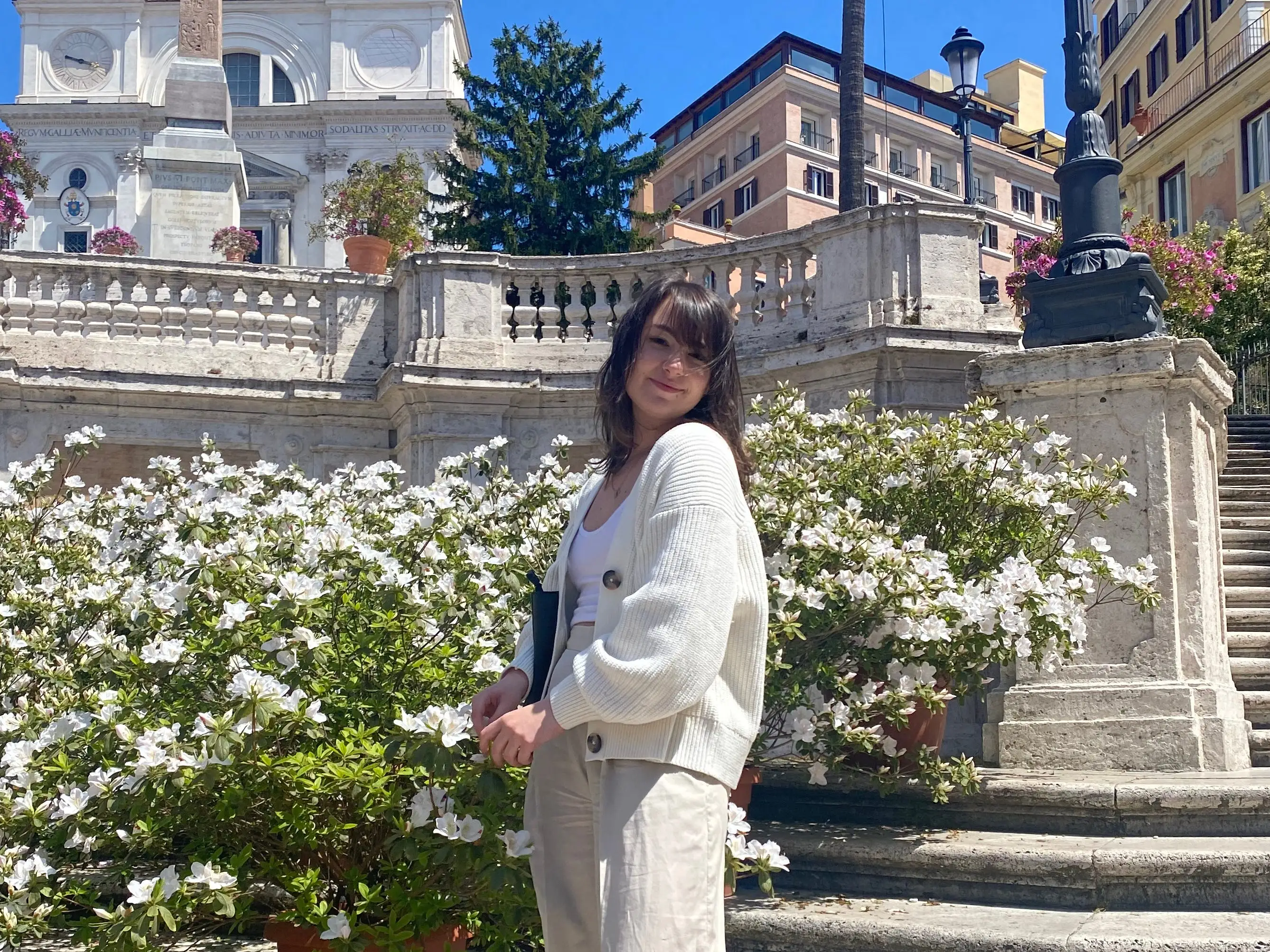 A woman wearing white posing at the foot of stairs.