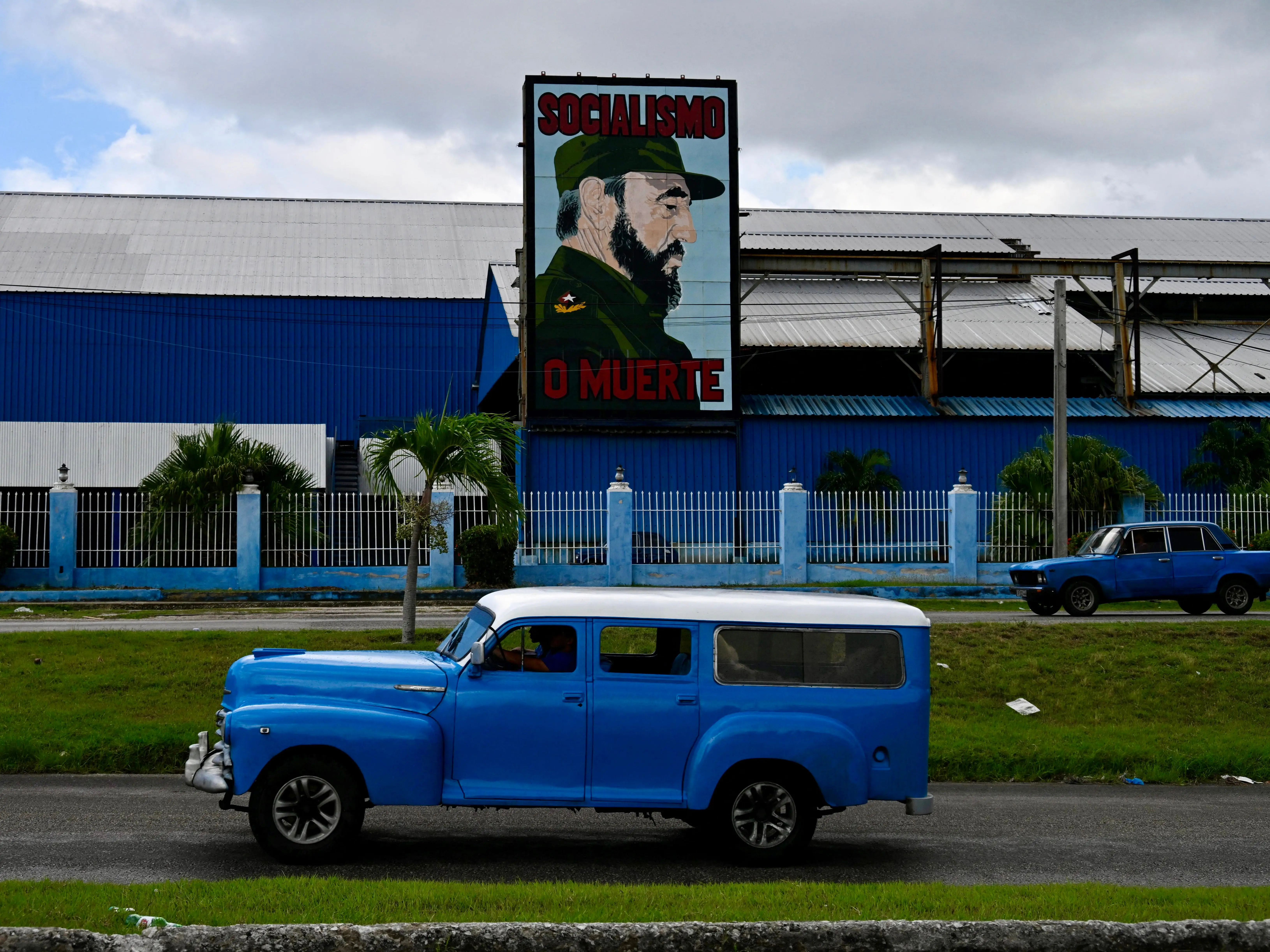 Old cars ride past a billboard with the portrait of late Cuban leader Fidel Castro that reads in spanish 'Socialism or Death' in Havana on August 11, 2025.