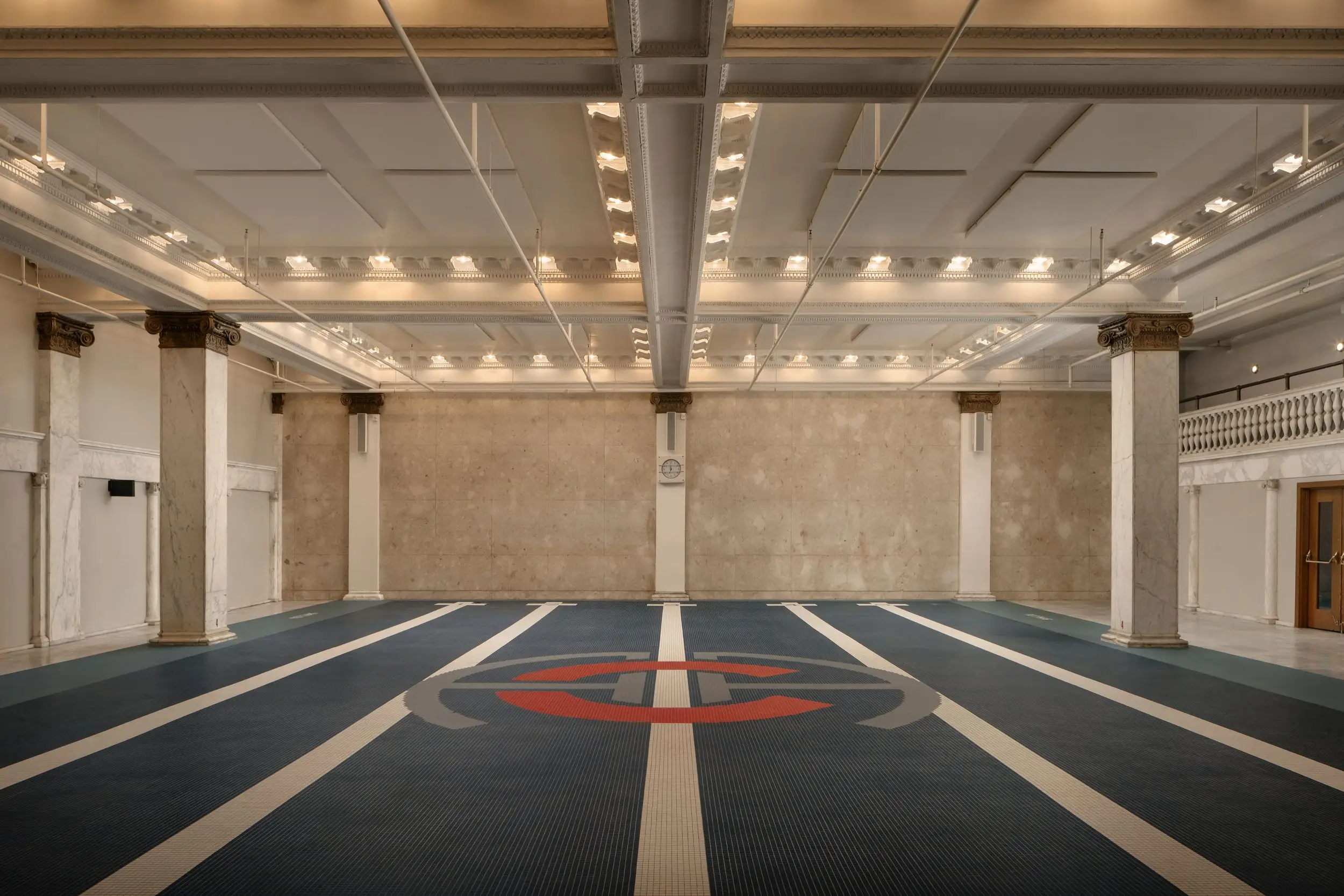 Empty grand interior hall with marble columns, ornate ceiling lighting, and a large roundel design on the floor.