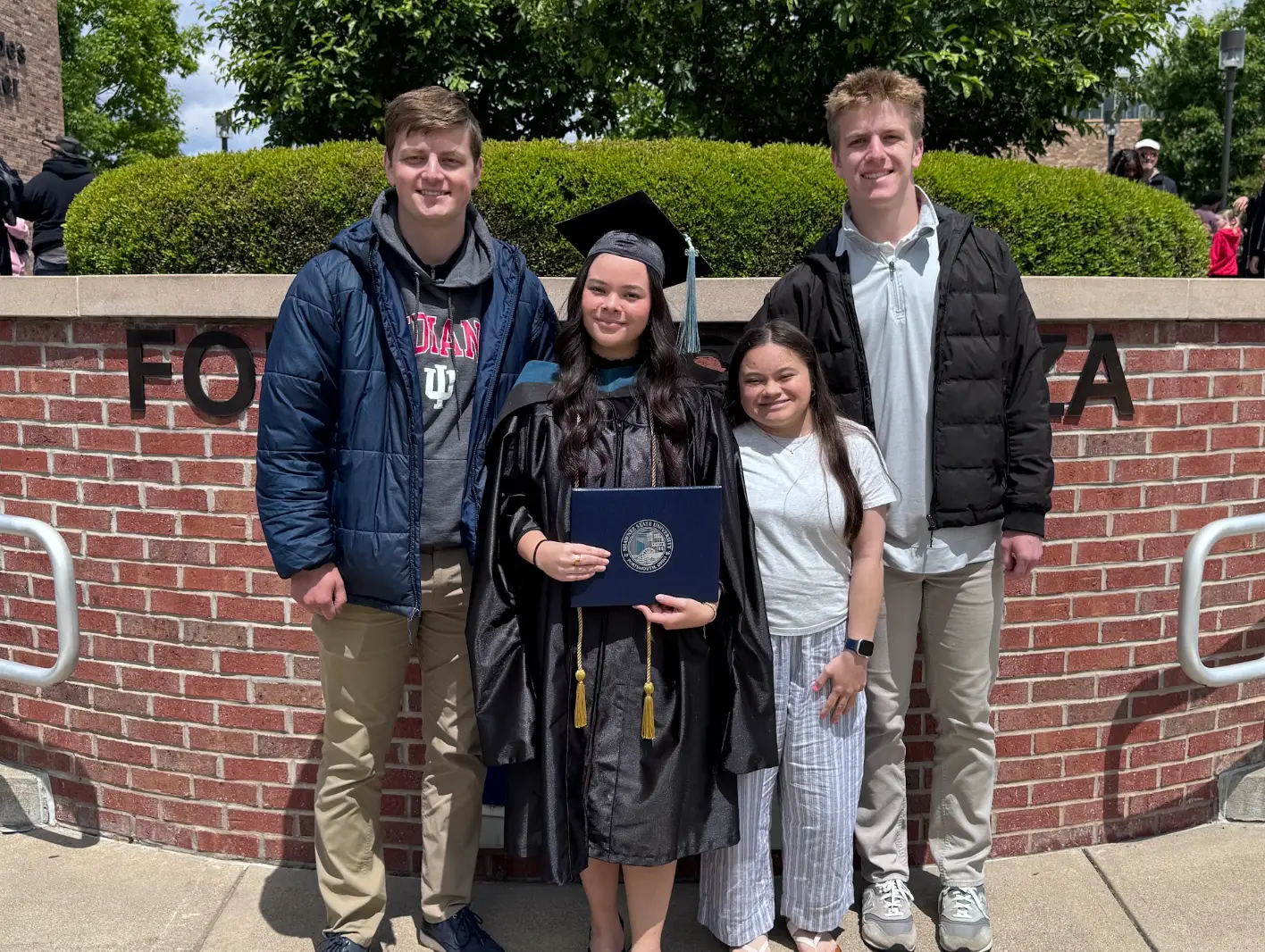 The writer's daughter stands next to her sister and brothers while holding a diploma and dressed in a cap and gown.