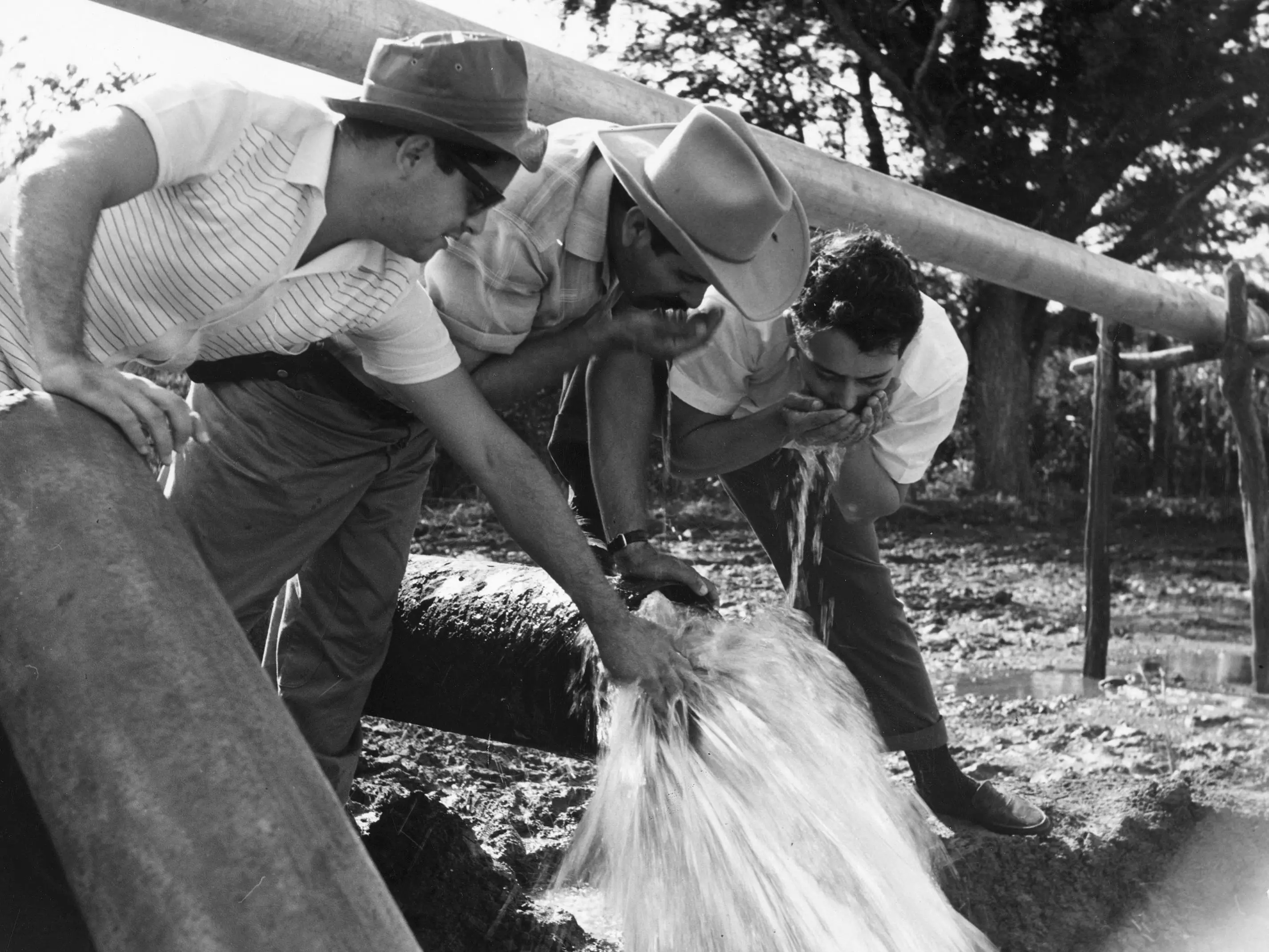 circa 1950: Cuban farmworkers take a drink of water from a water pump used for irrigating the land.