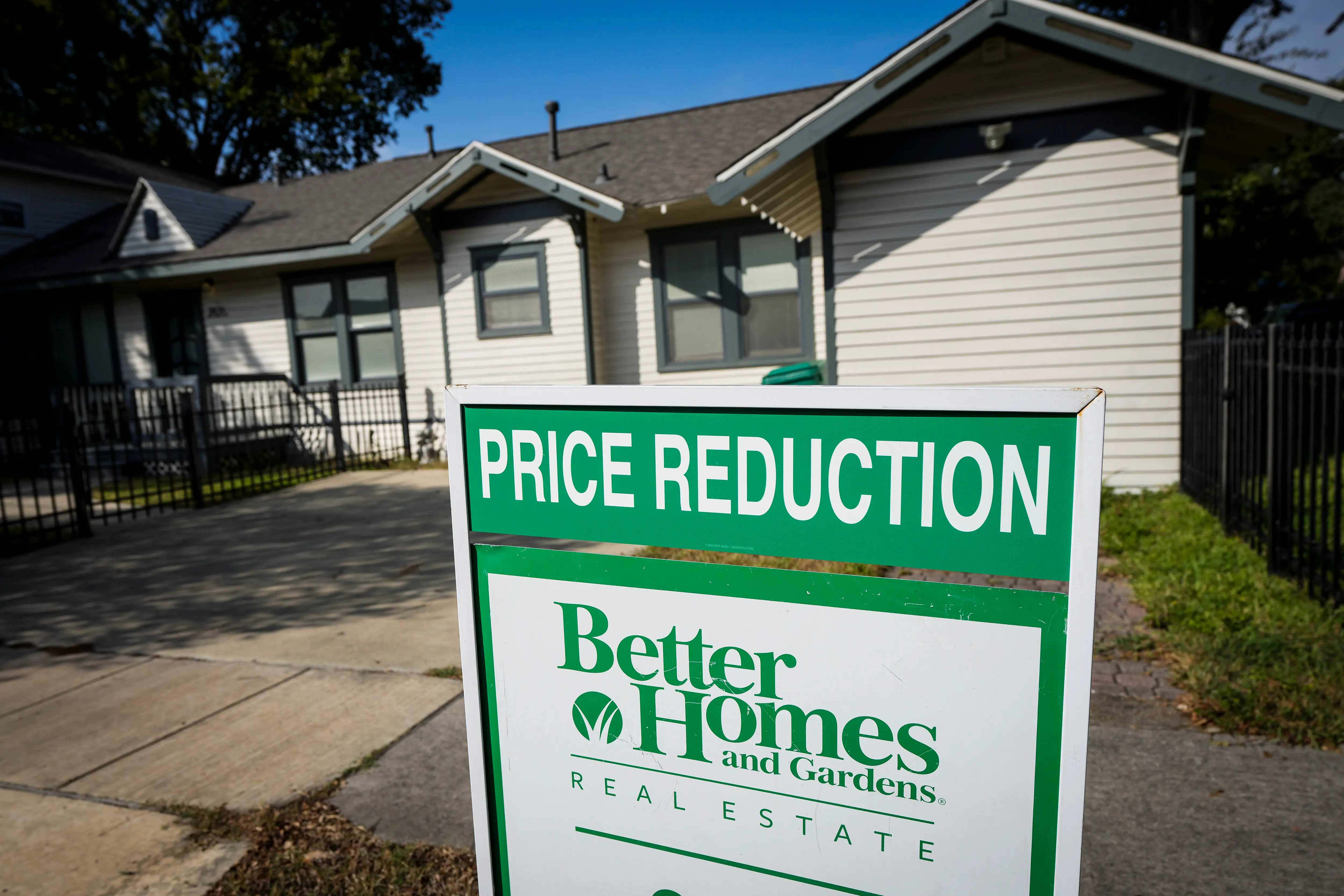 A “PRICE REDUCTION” Better Homes and Gardens Real Estate sign stands in front of a residential house.