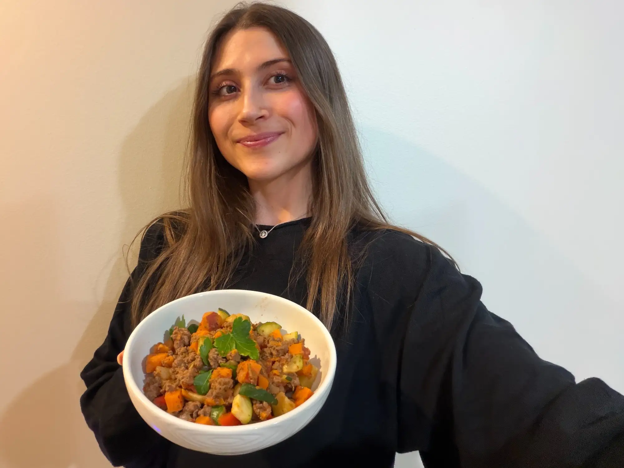 Woman smiling, holding bowl of ground meat, veggies