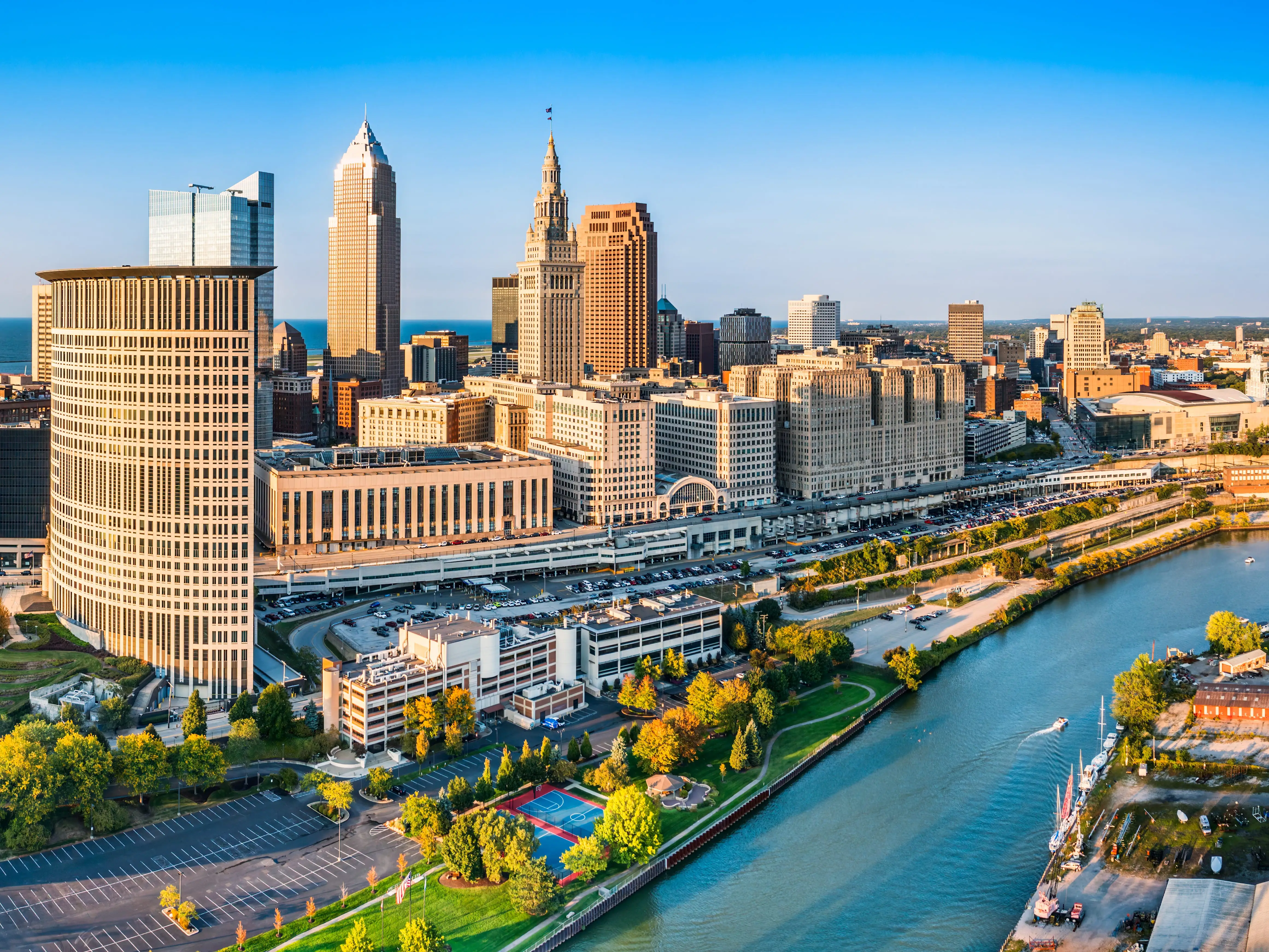 Downtown Cleveland skyline rises beside the Cuyahoga River with Terminal Tower and waterfront parks in warm light.