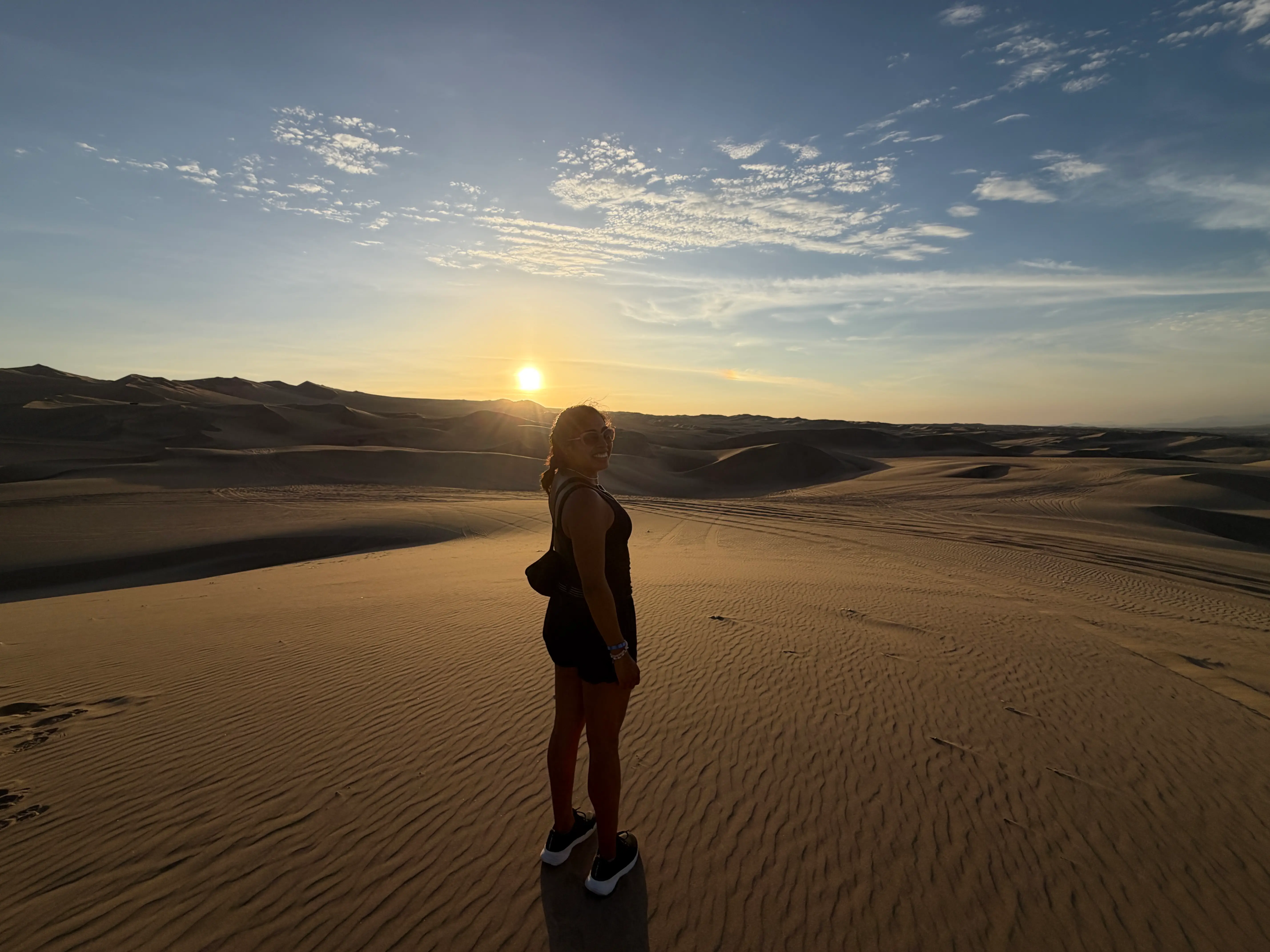 A woman standing on the sand with a sunset in the background.