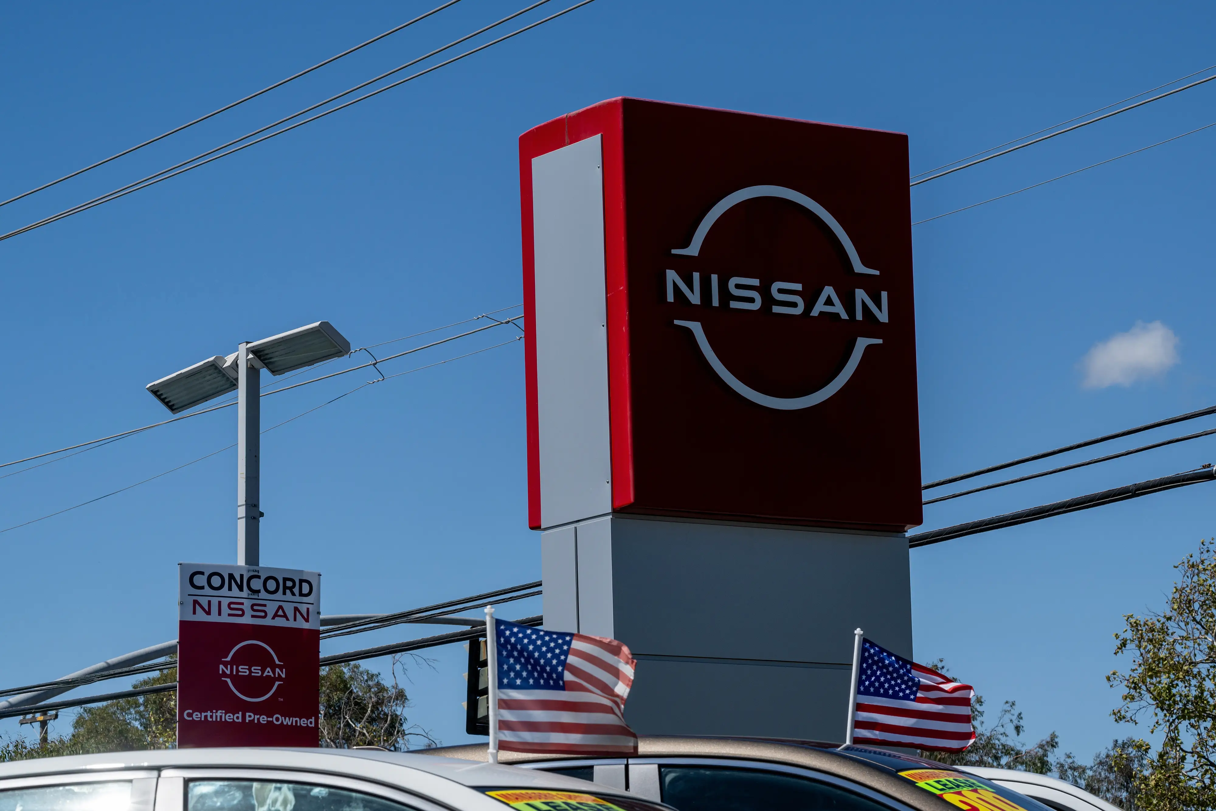 A Nissan dealership with used cars flying American flags from their driver-side windows.