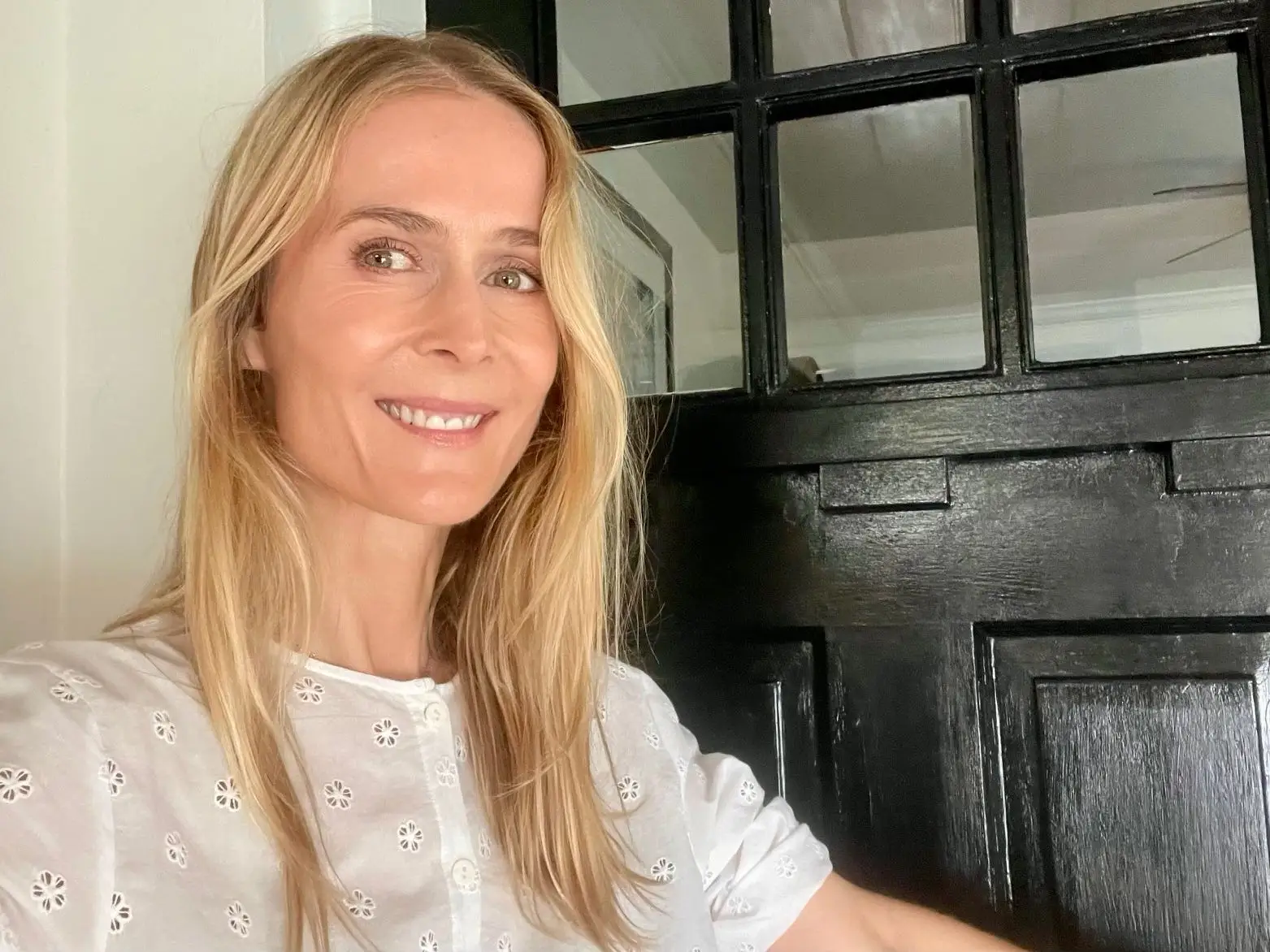 The author smiling in front of a black doorway, wearing a white top.