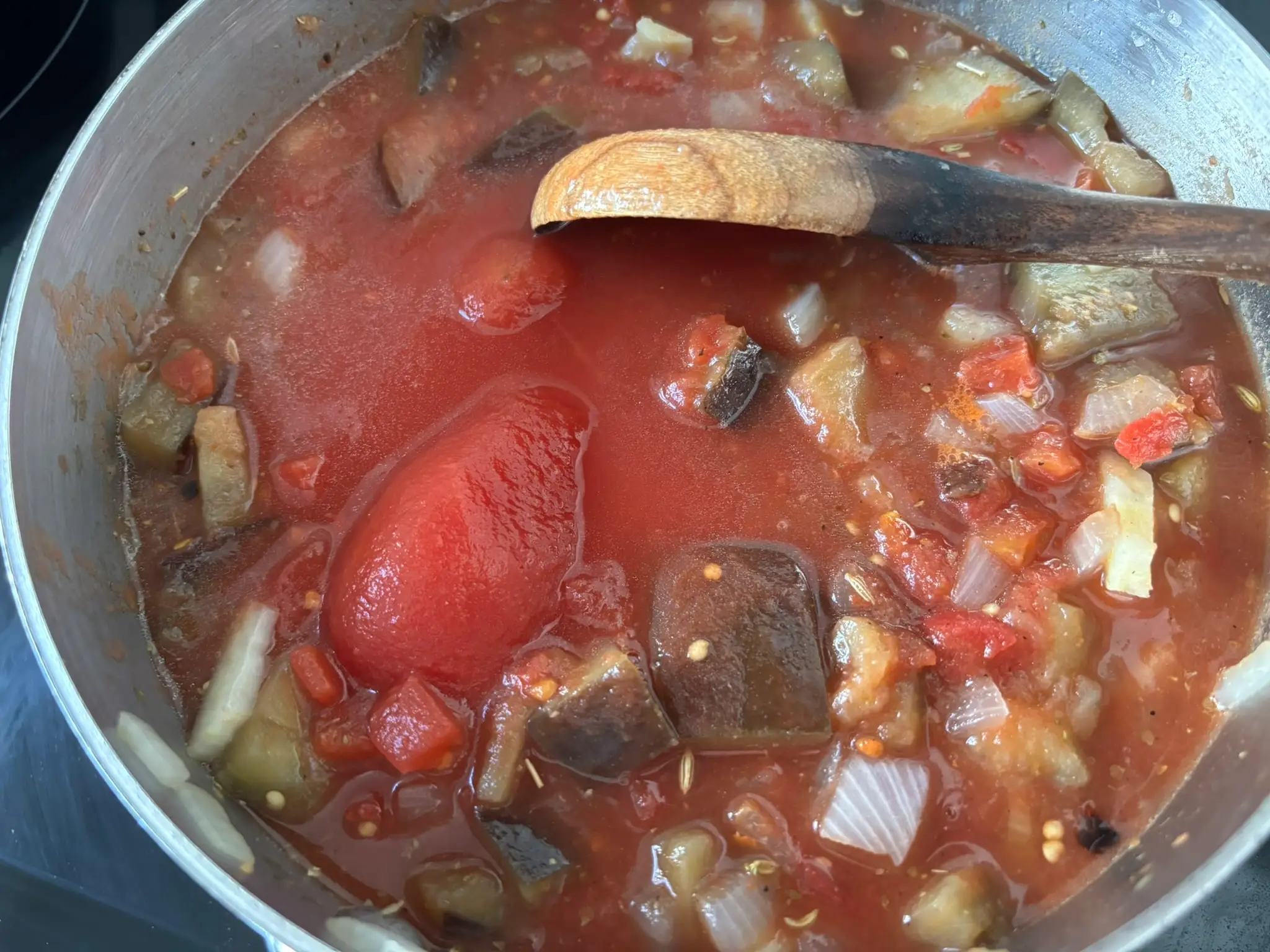 The writer is mixing tomatoes in a pot with a wooden spoon to make soup.