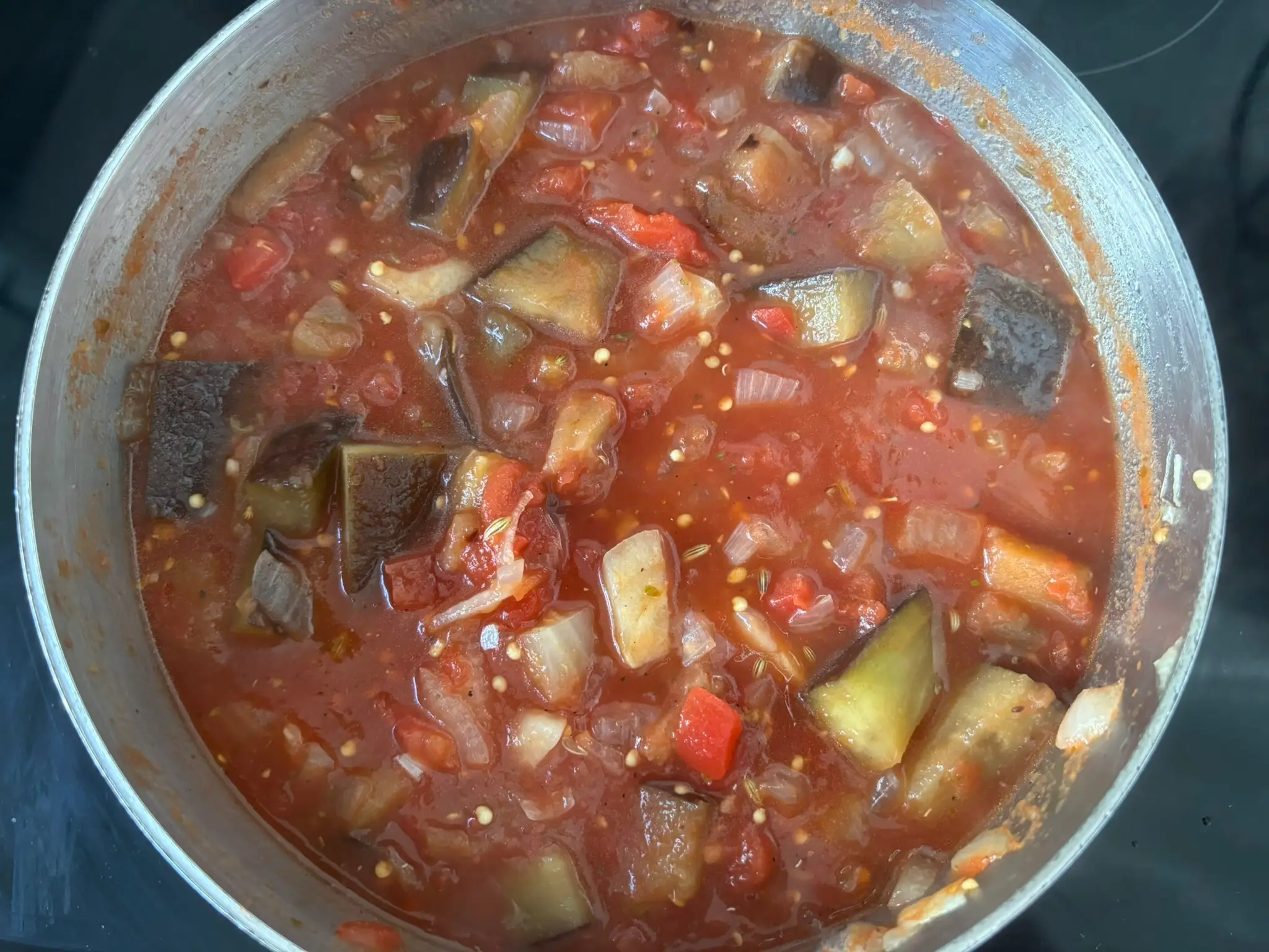 A tomato and eggplant soup simmers in a pot on the stove.