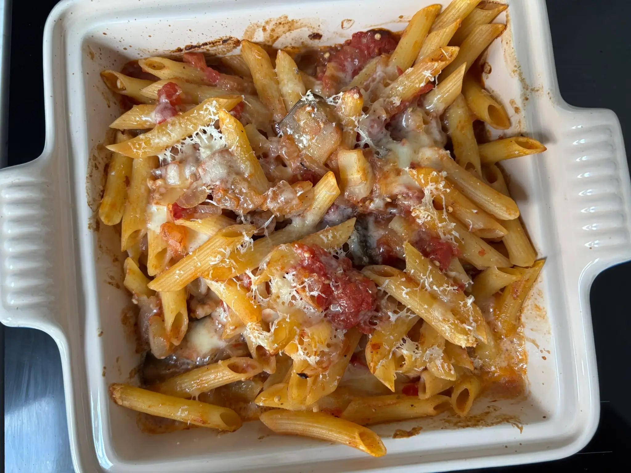 Baked penne pasta with tomato and eggplant sits in a white square casserole dish.