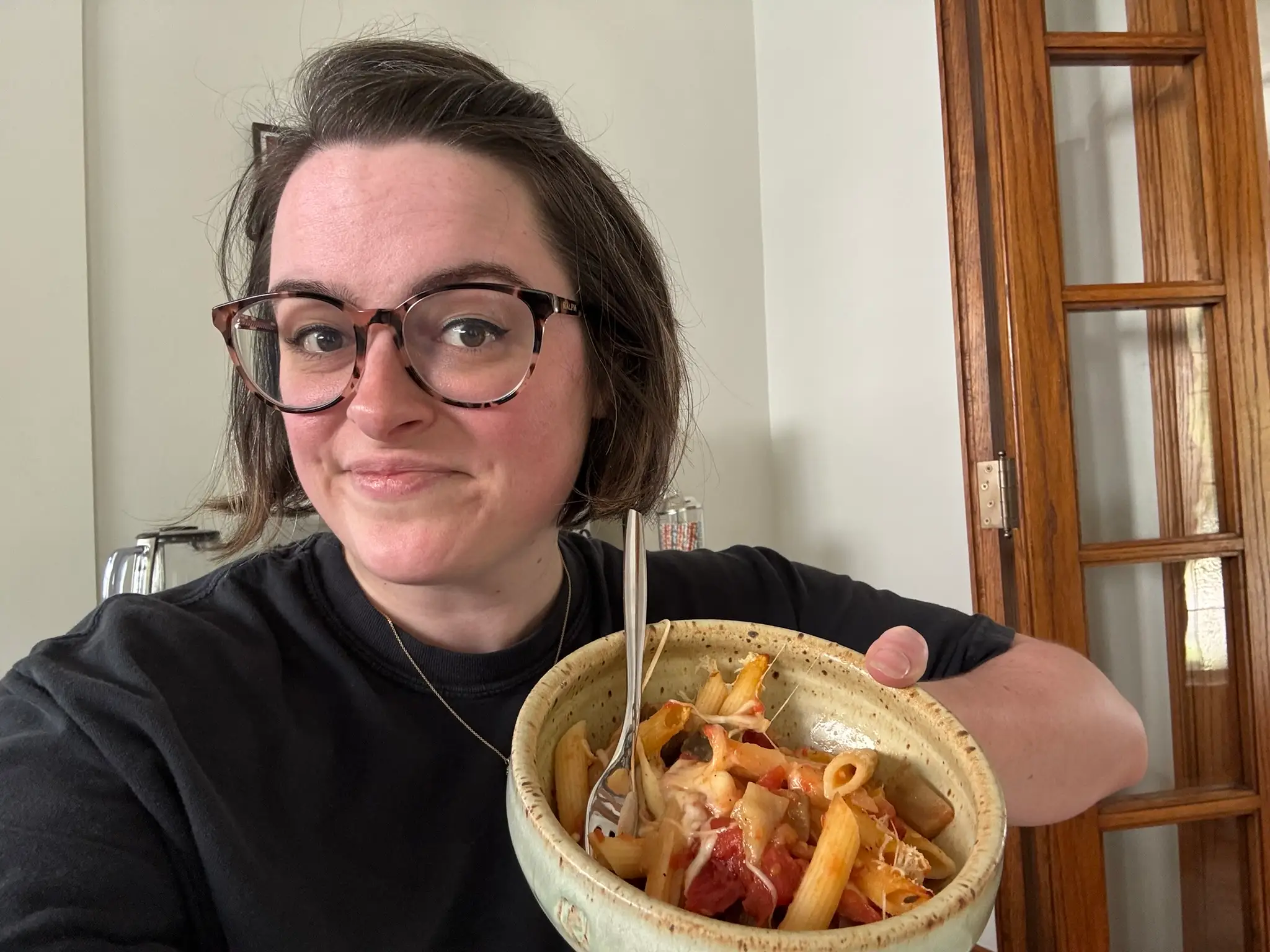 The writer is holding a bowl of baked pasta with tomatoes and eggplant.
