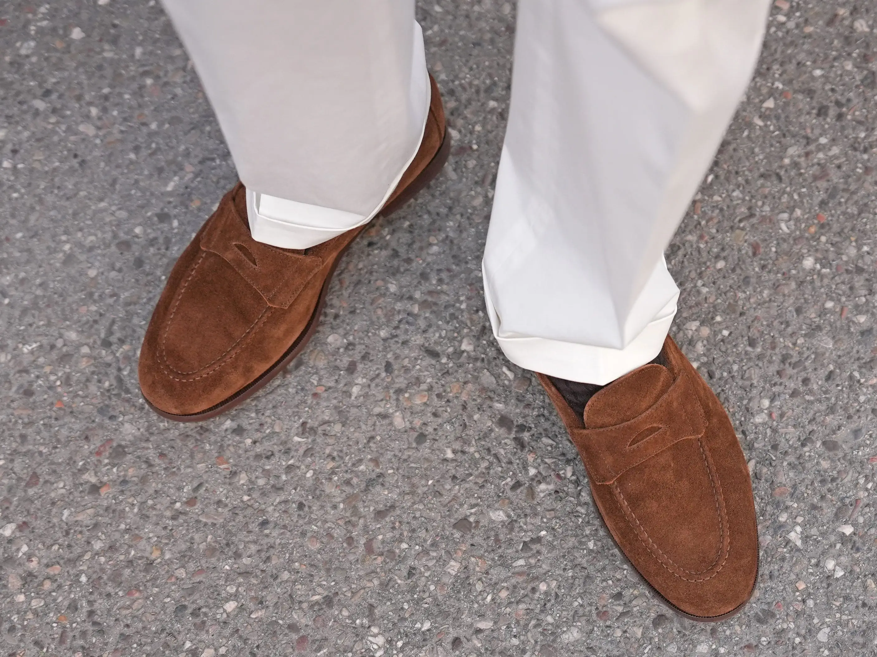 A person wearing a pair of brown suede loafers.