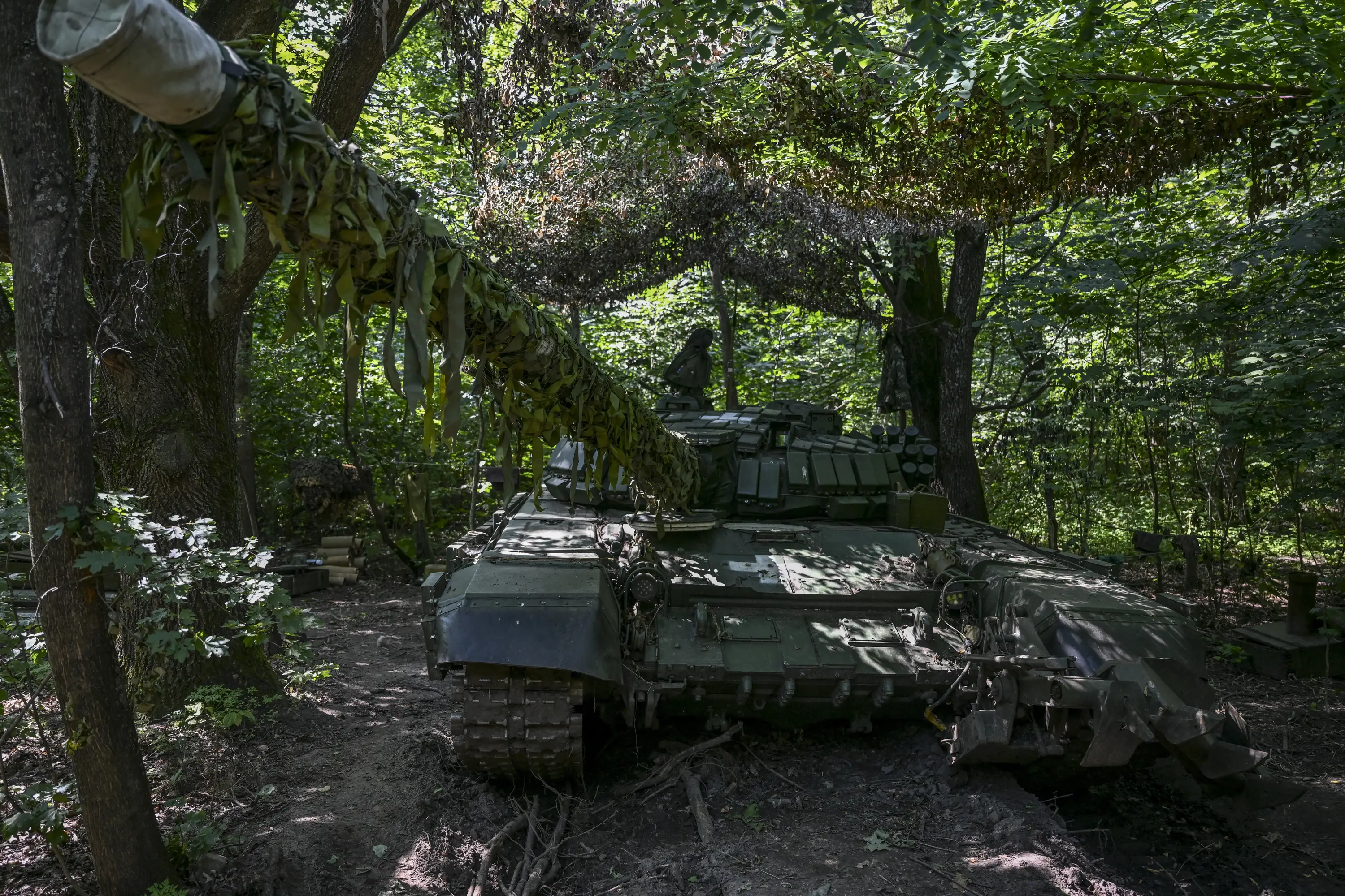 A captured Russian tank with explosive reactive armor sits udner camouflaged netting.
