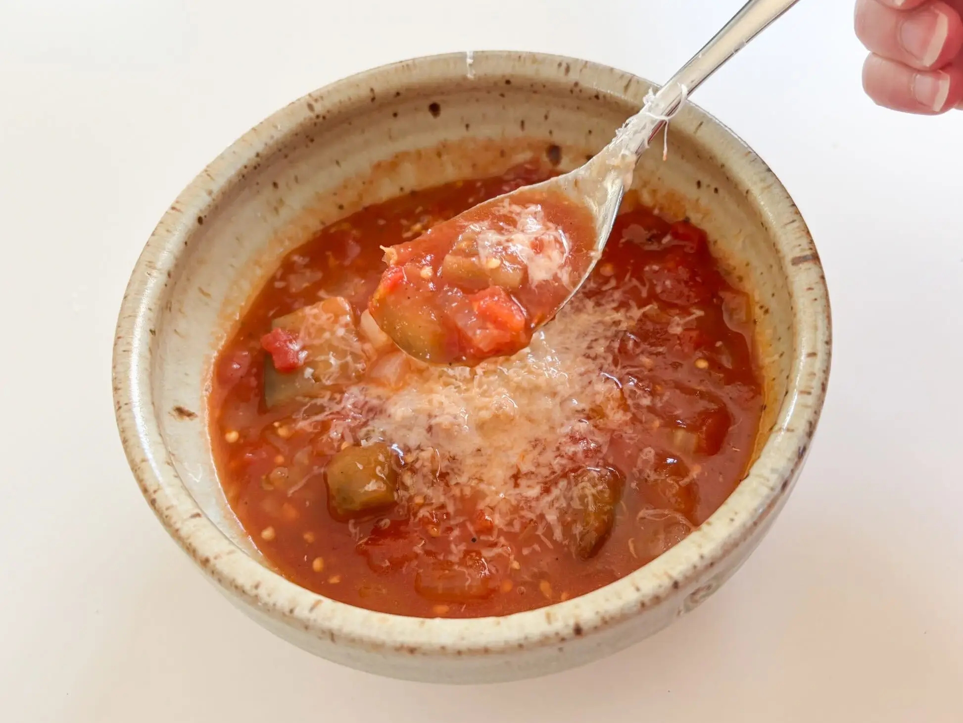 The writer lifts a spoonful of chunky tomato soup with grated cheese from a ceramic bowl.