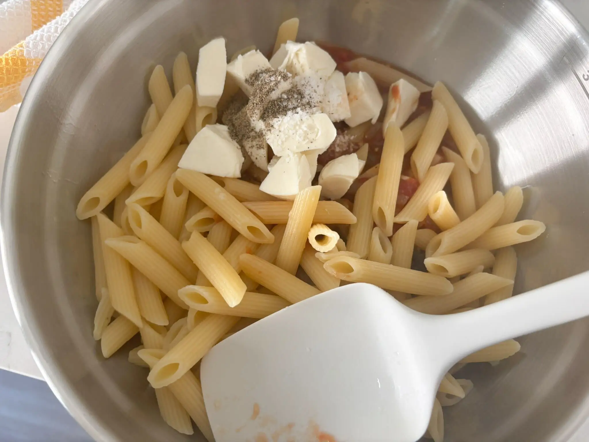 Penne pasta with tomato-eggplant soup, mozzarella, and black pepper in a stainless steel mixing bowl.