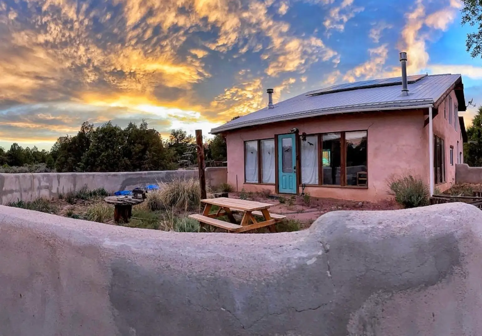 The writer's pink off-grid house in New Mexico, with a sunset in the background and a picnic table nearby.