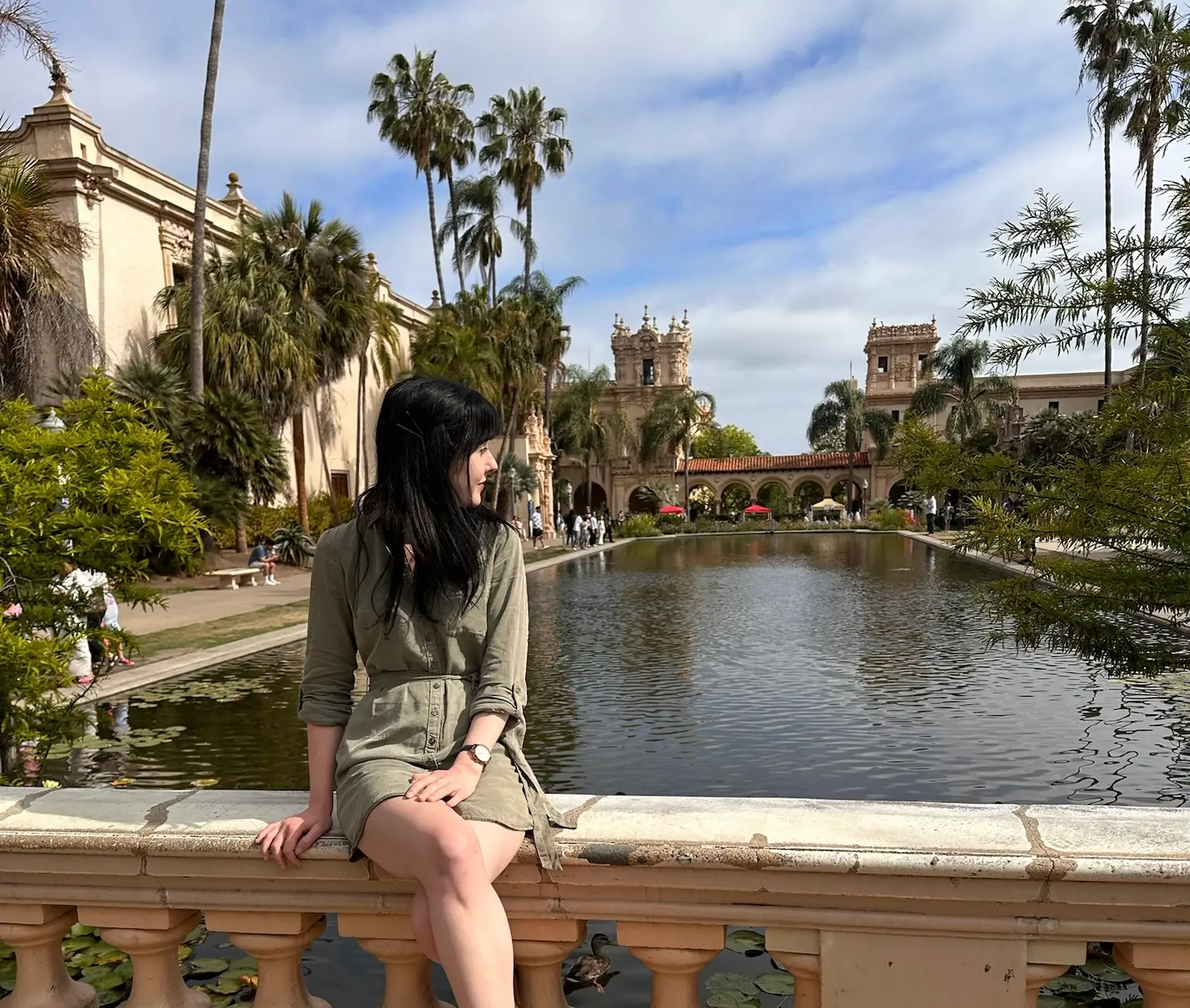 Woman sitting on ledge near palm trees water,