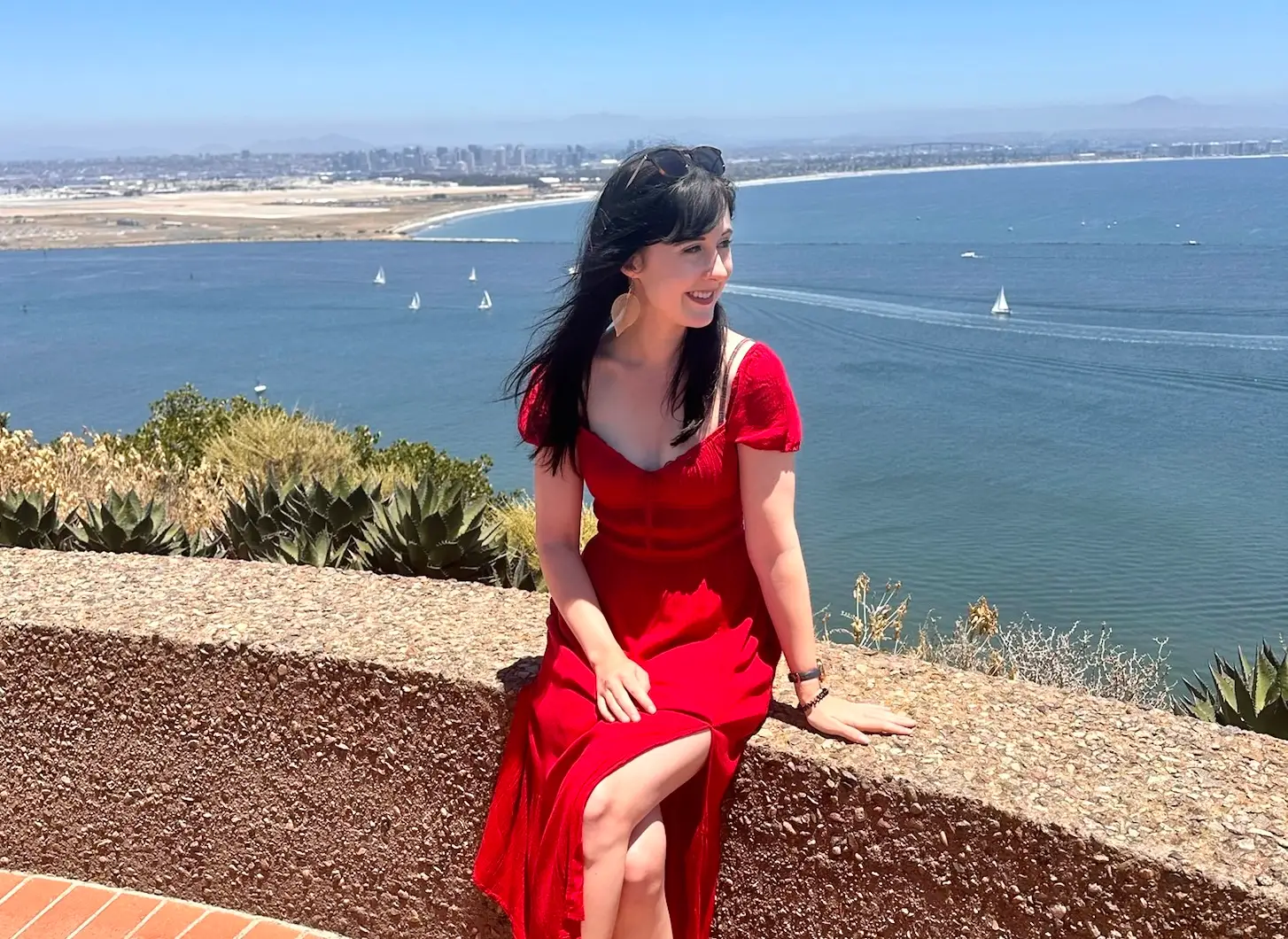 Woman in red dress posing on ledge near water