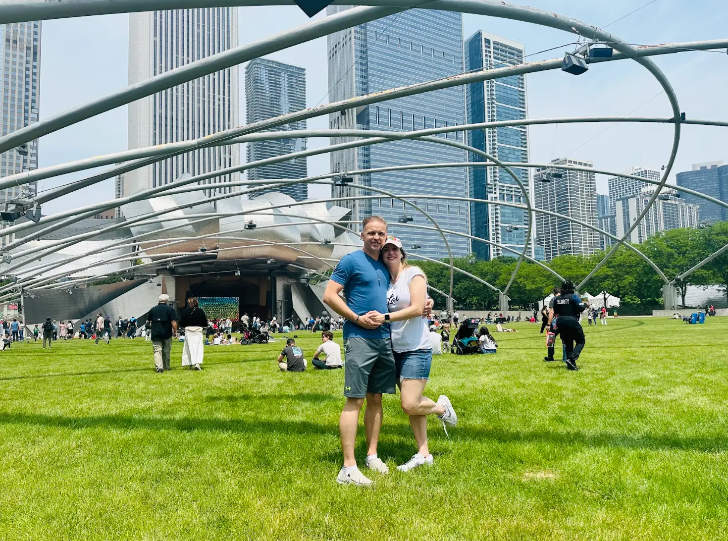 The writer and her partner hold hands and pose in front of an outdoor stage in the grass in Chicago.