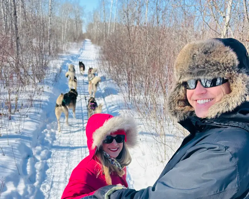 The writer and her partner sledding with a pack of dogs in snowy woods in Canada.