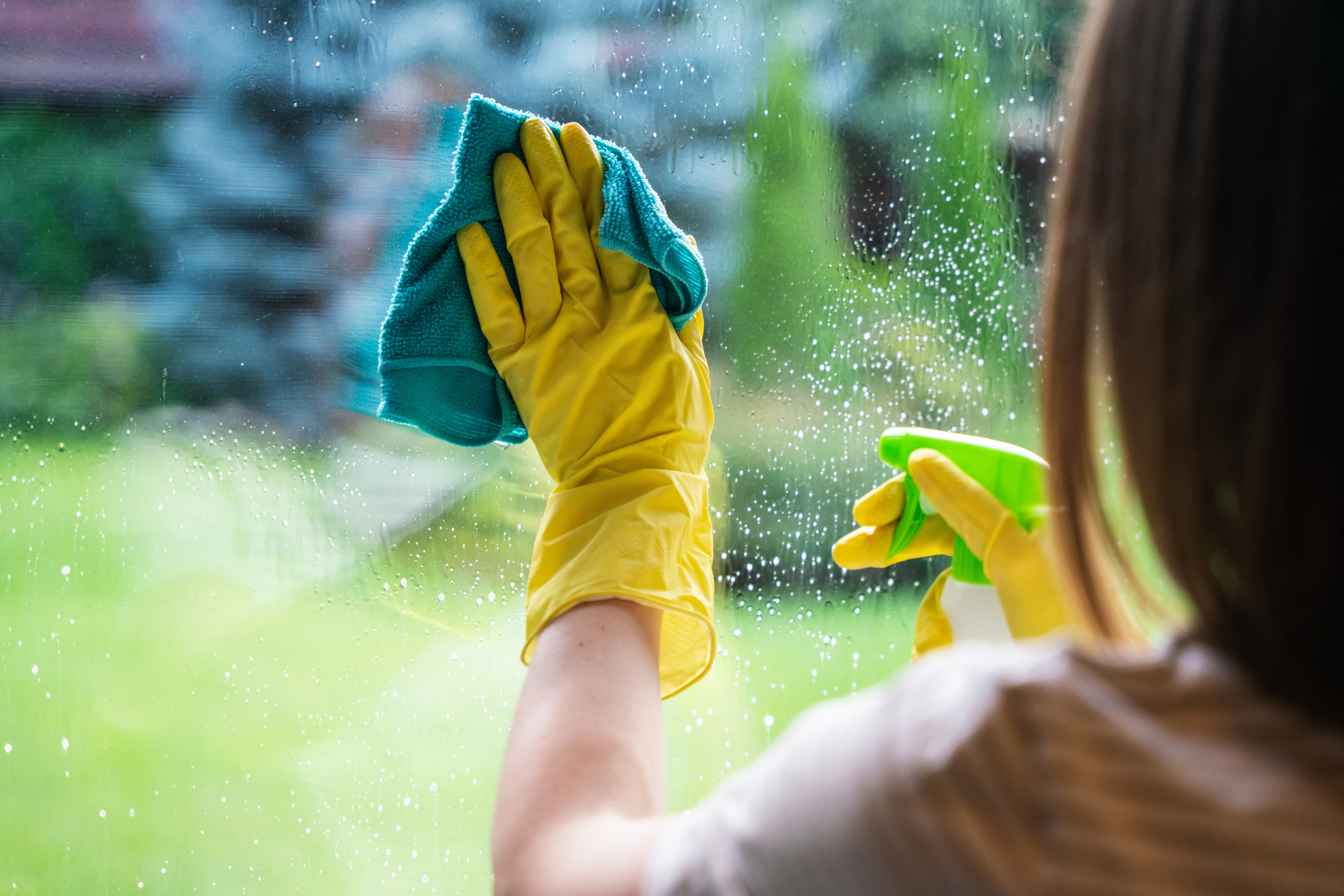 A woman is cleaning a window while wearing yellow gloves.