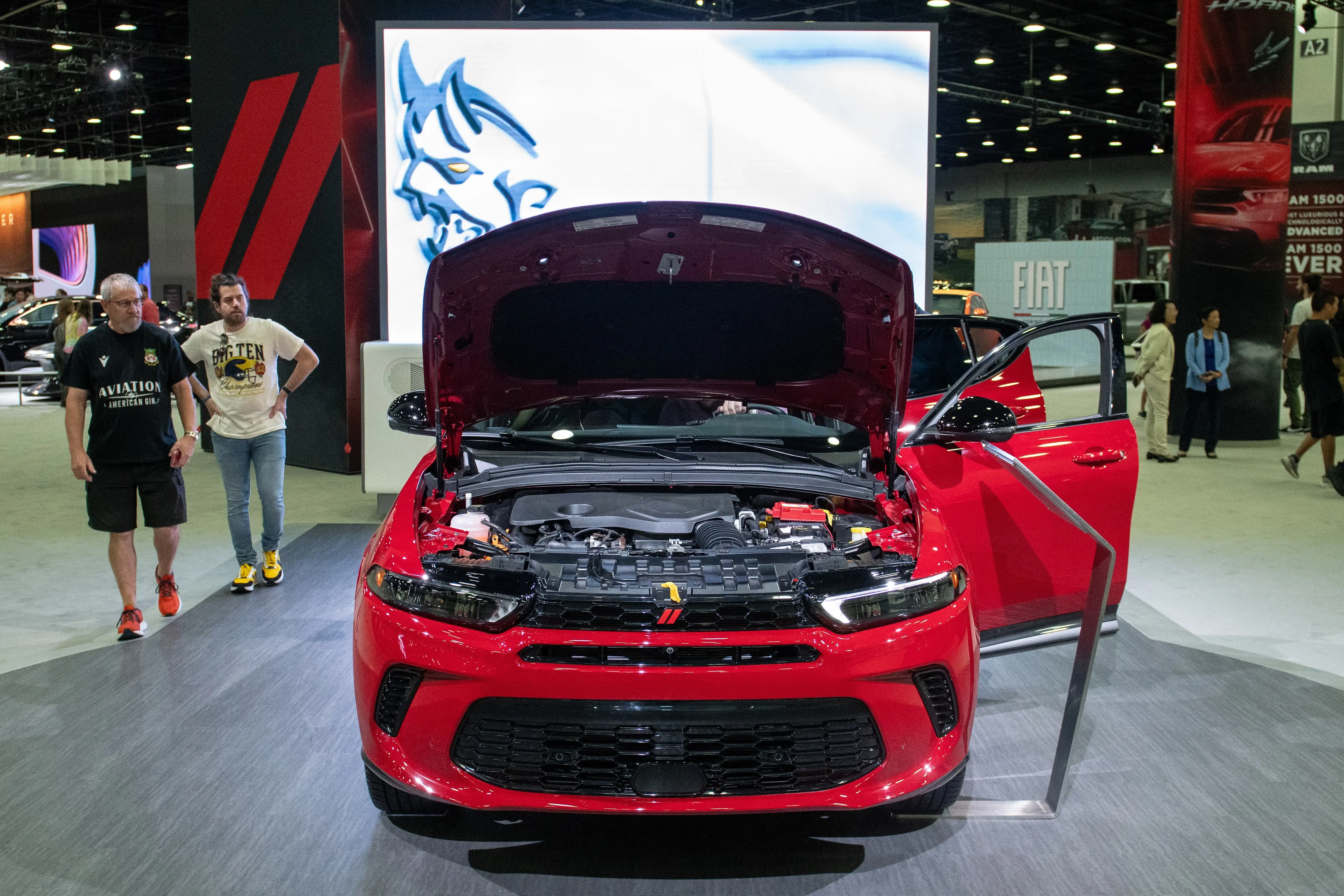 People walk around a red Dodge Hornet during an auto show. The SUV's hood is open.