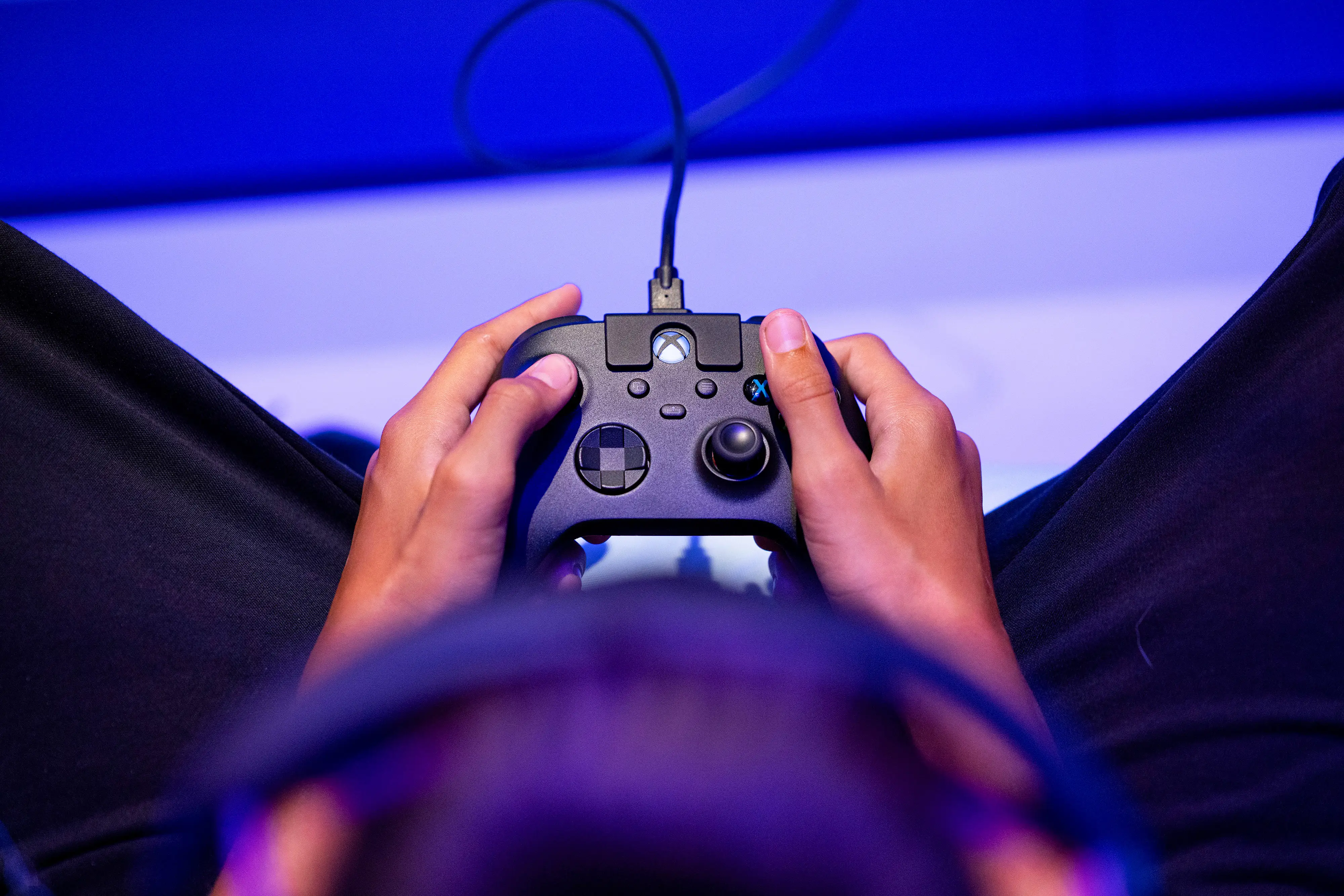 A person, wearing a headset, holds onto an Xbox controller.