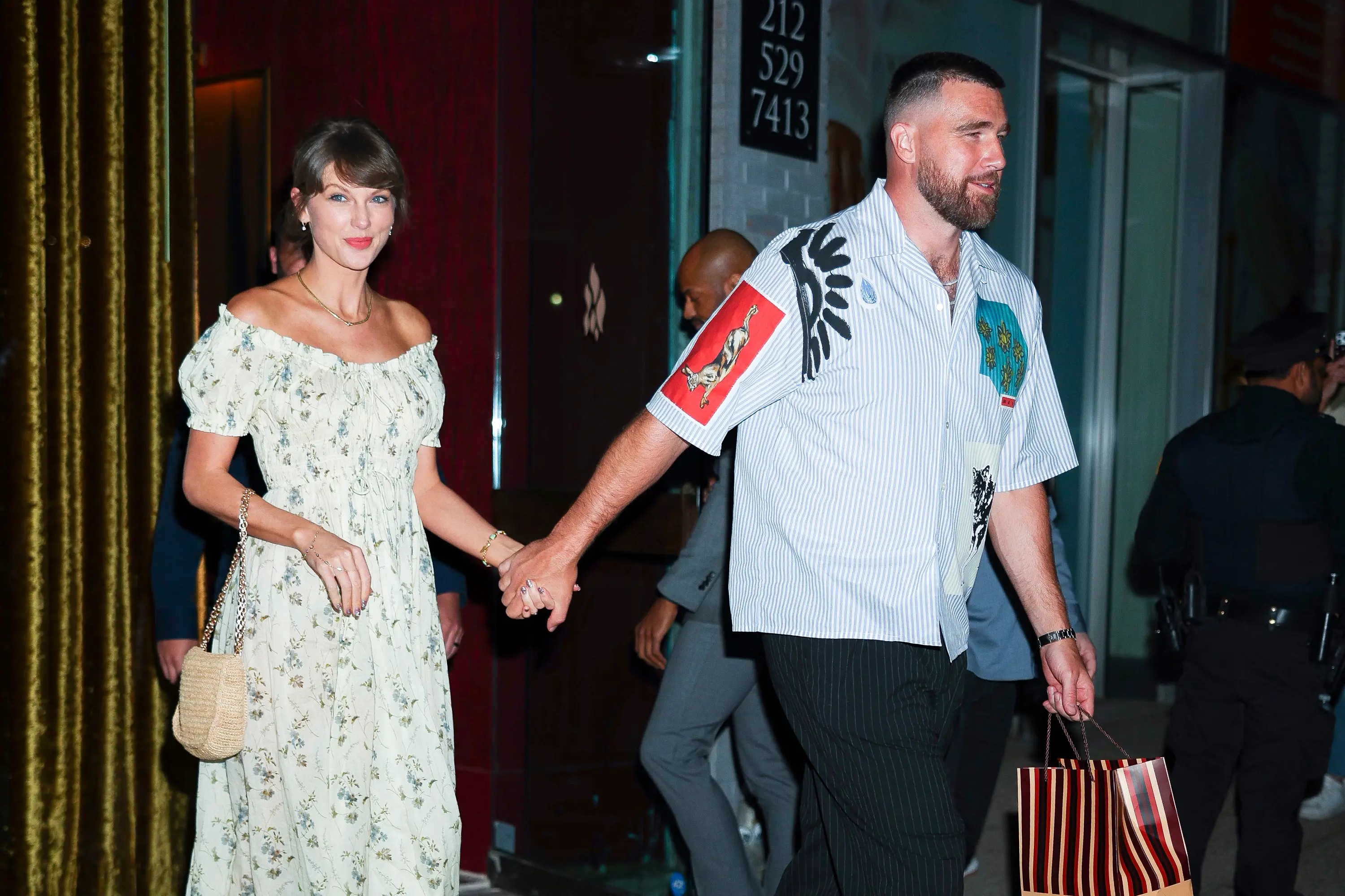 Taylor Swift and Travis Kelce hold hands while leaving a city venue at night.
